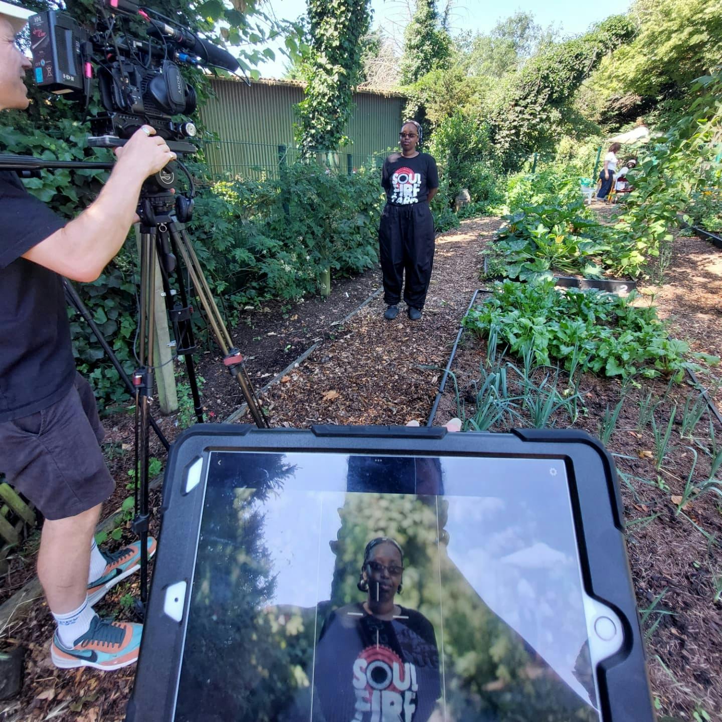 Community Garden, Earth Tenders' founder stands in front of a camera