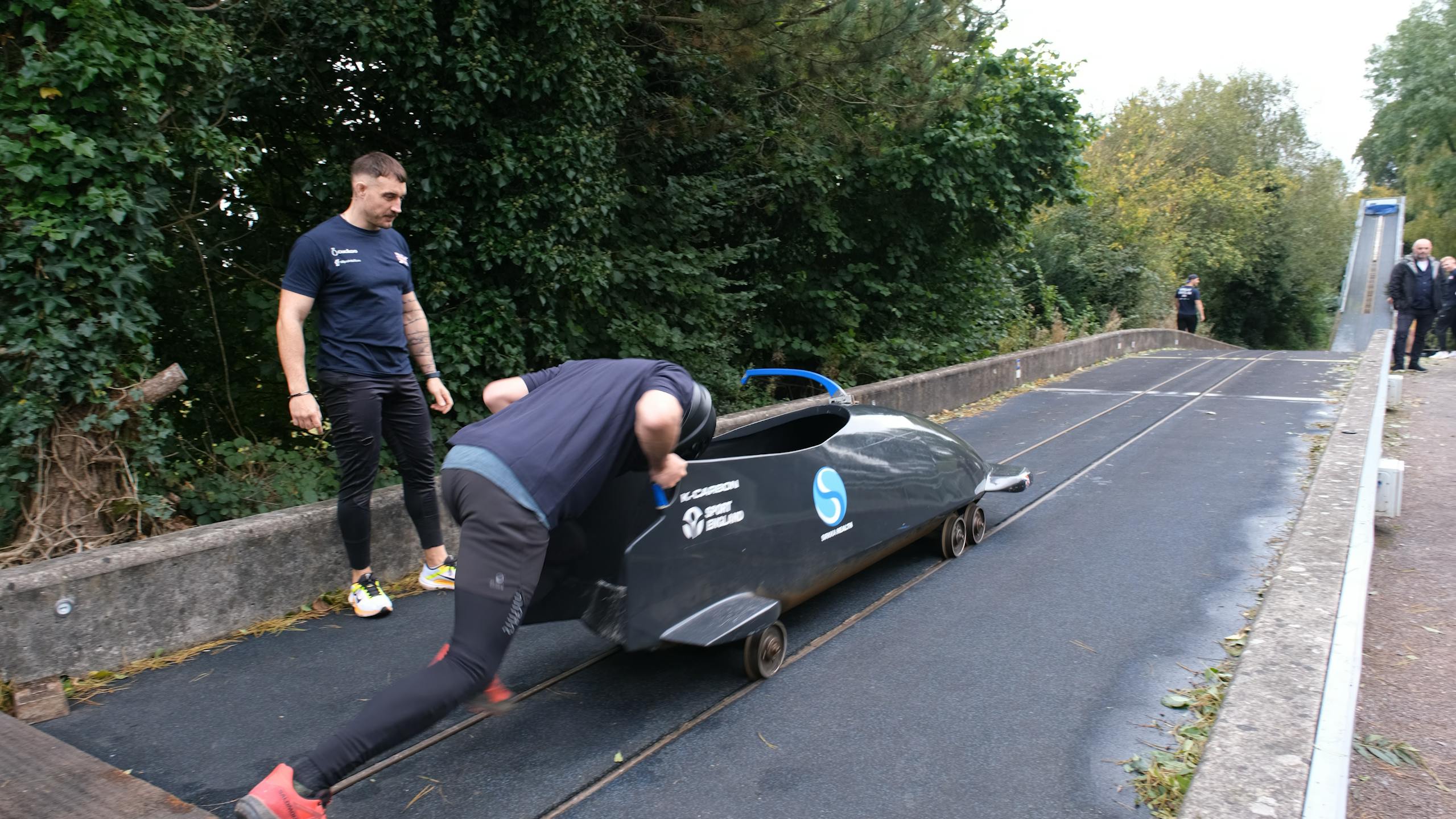 Under the watchful eye of Team GB Pilot, Adam Baird, Cuckoo CEO, Paul Hellings pushes Bobsleigh on a dry track.