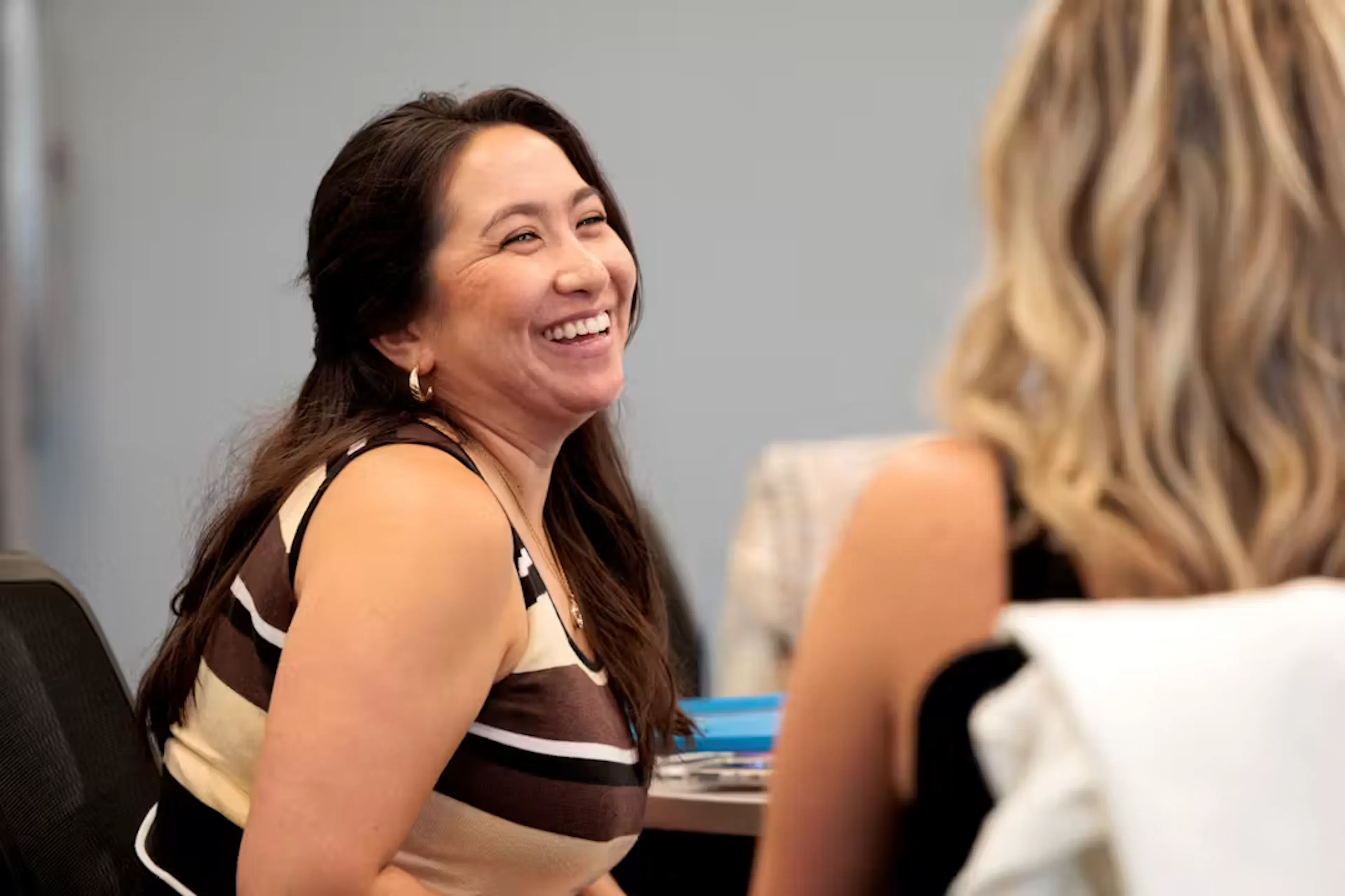 Woman smiling and talking with another woman sitting at a table.