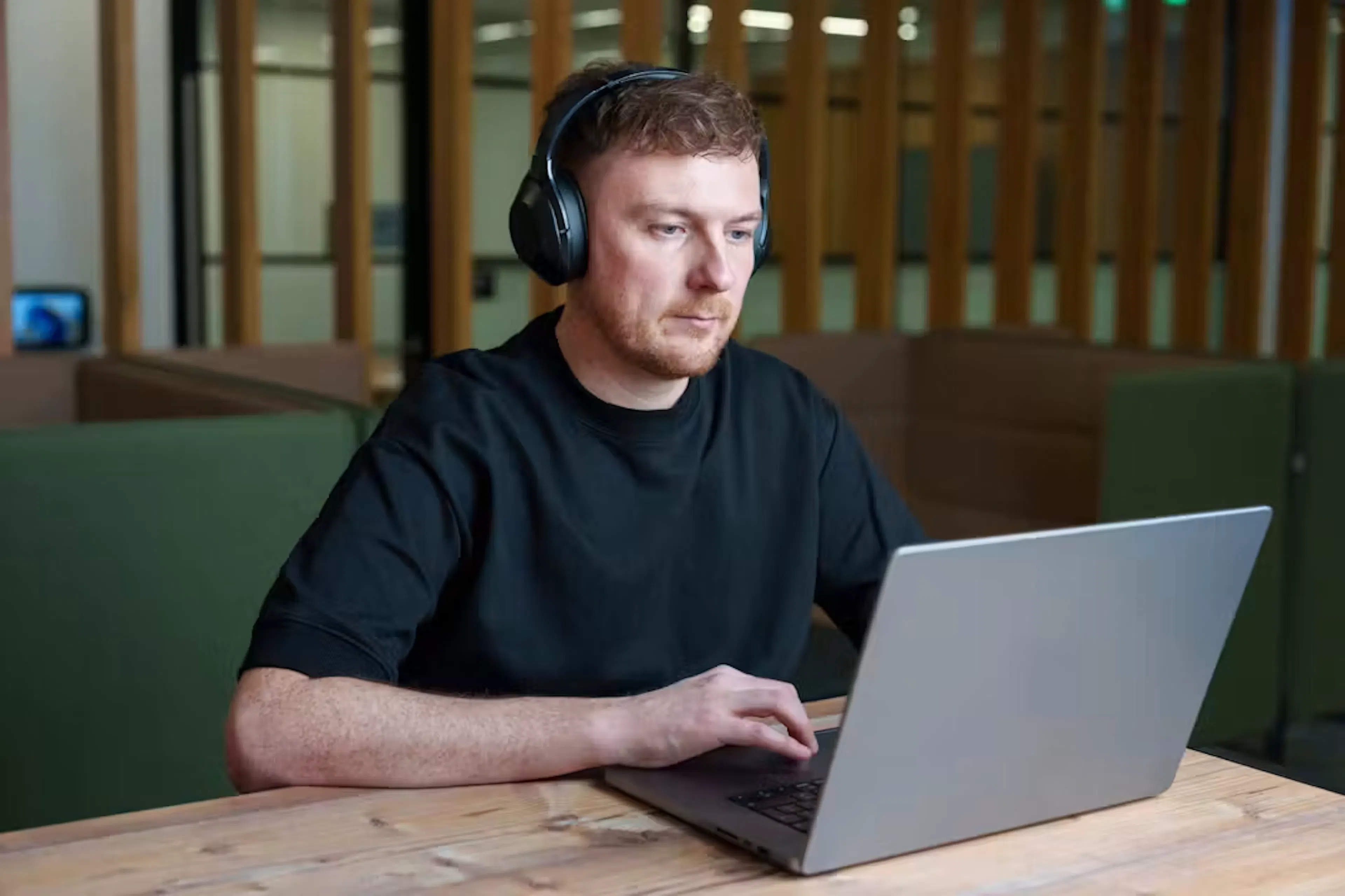 A individual sitting at a desk wearing headphones, looking at a laptop