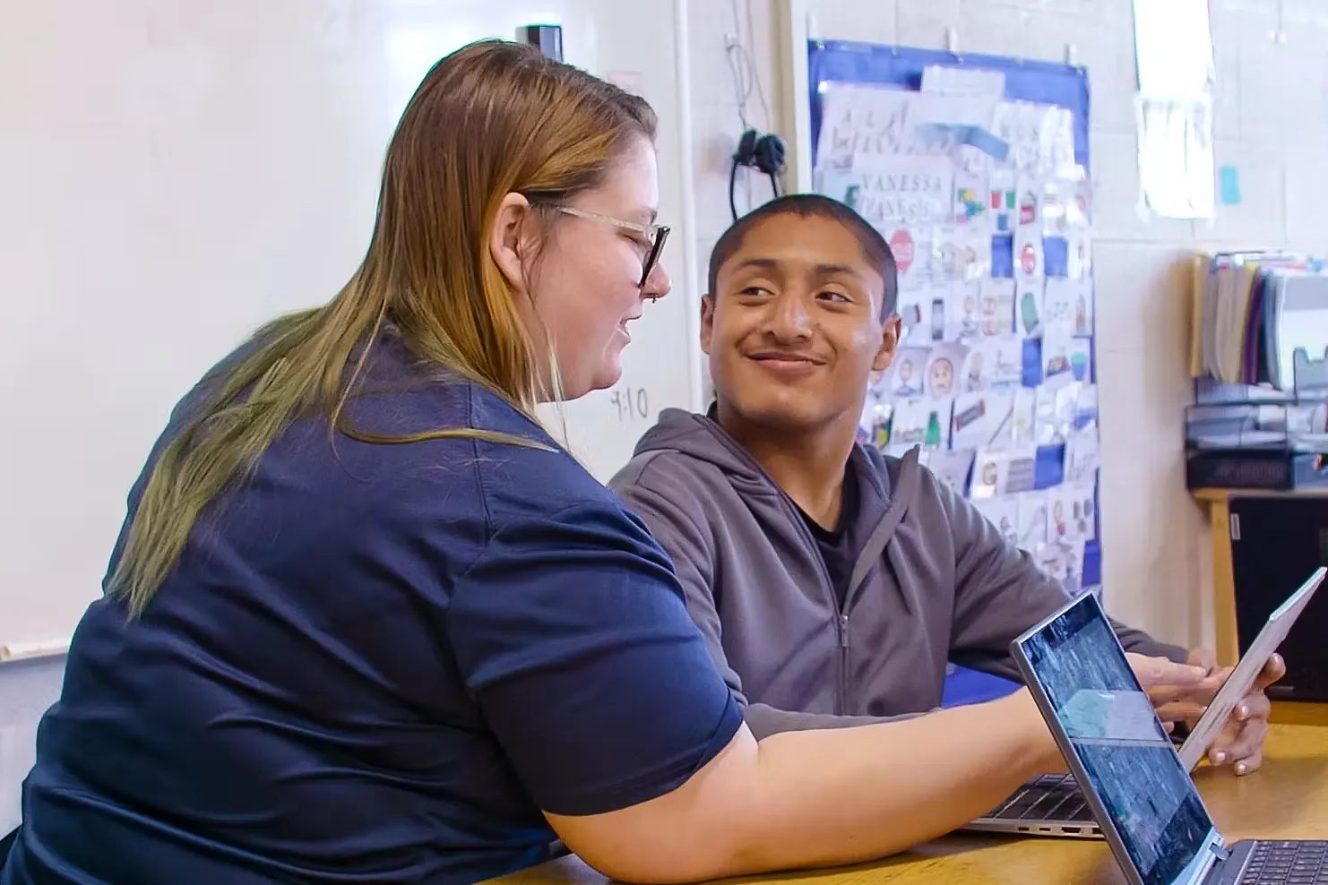 A teacher helping a student on a laptop