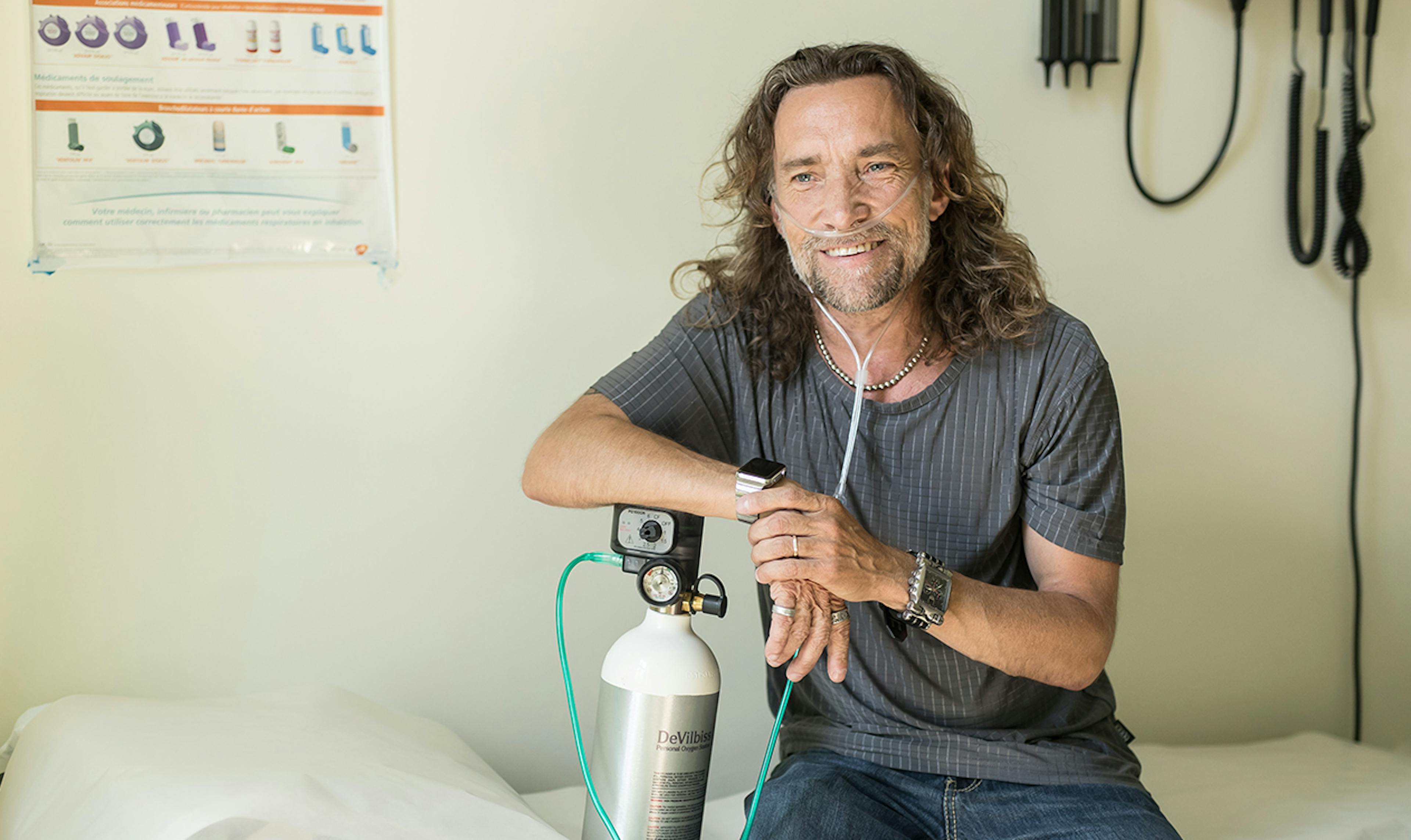 Man in doctor's office leans on his oxygen tank.