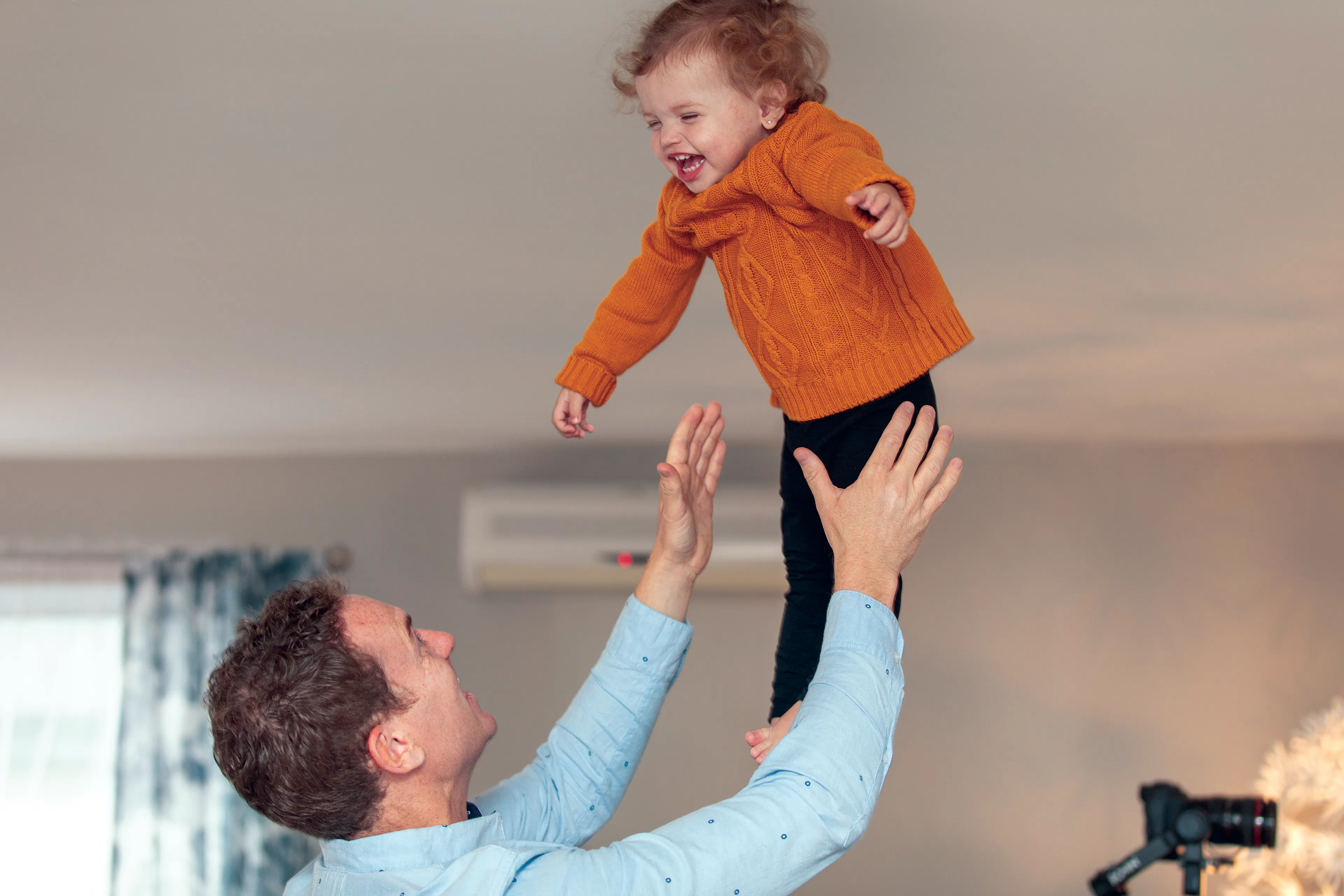 A father throw's his two year old son in the air, the son is laughing 