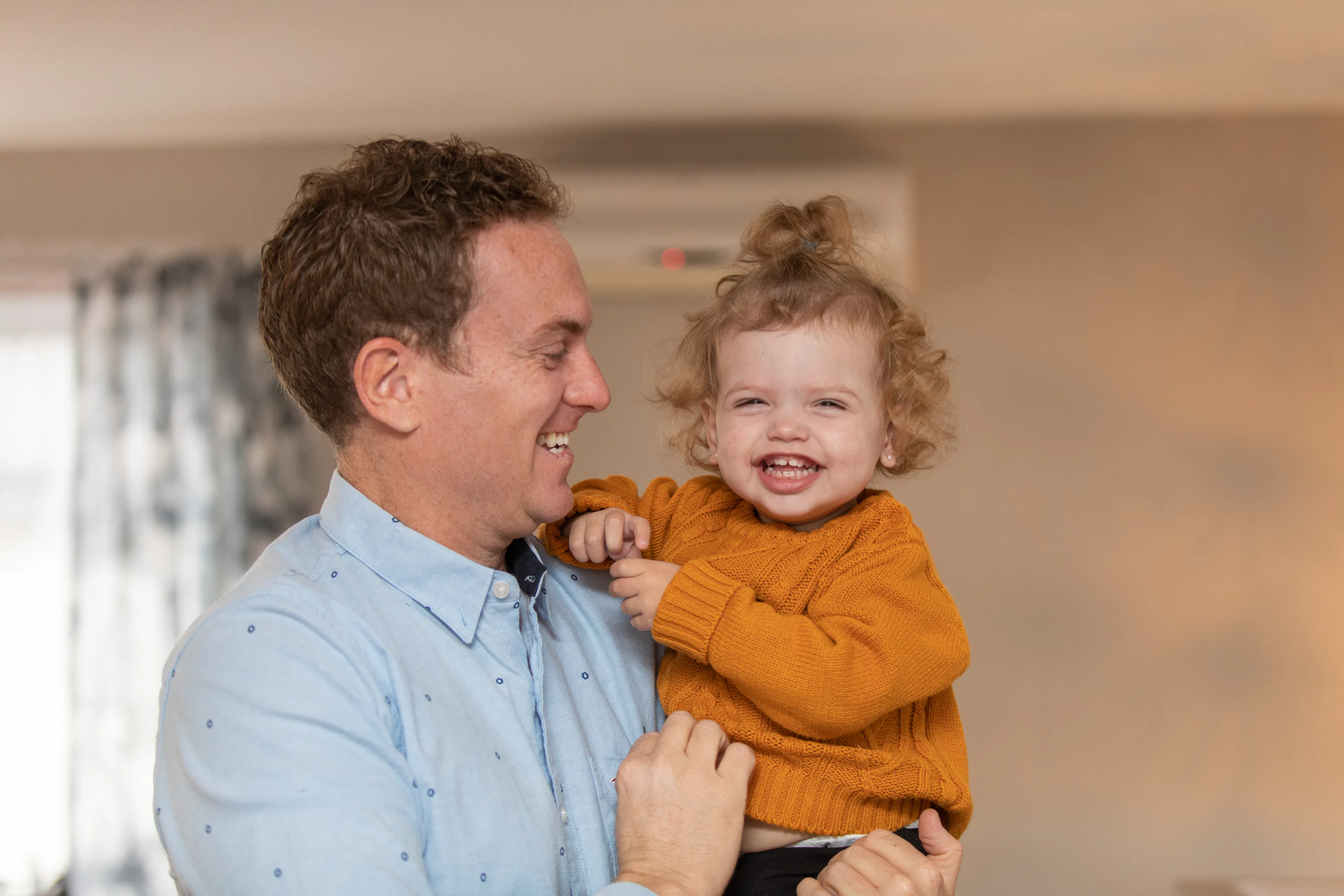 A father holds his young toddler daughter in his arms as she smiles 