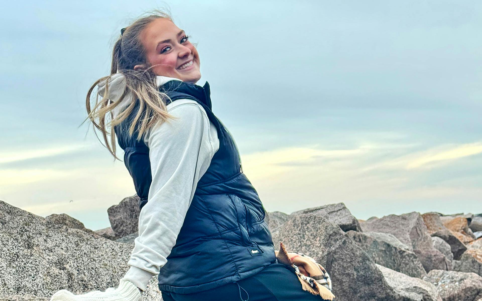 Alexie Babin est assise sur de gros rochers devant un ciel bleu.