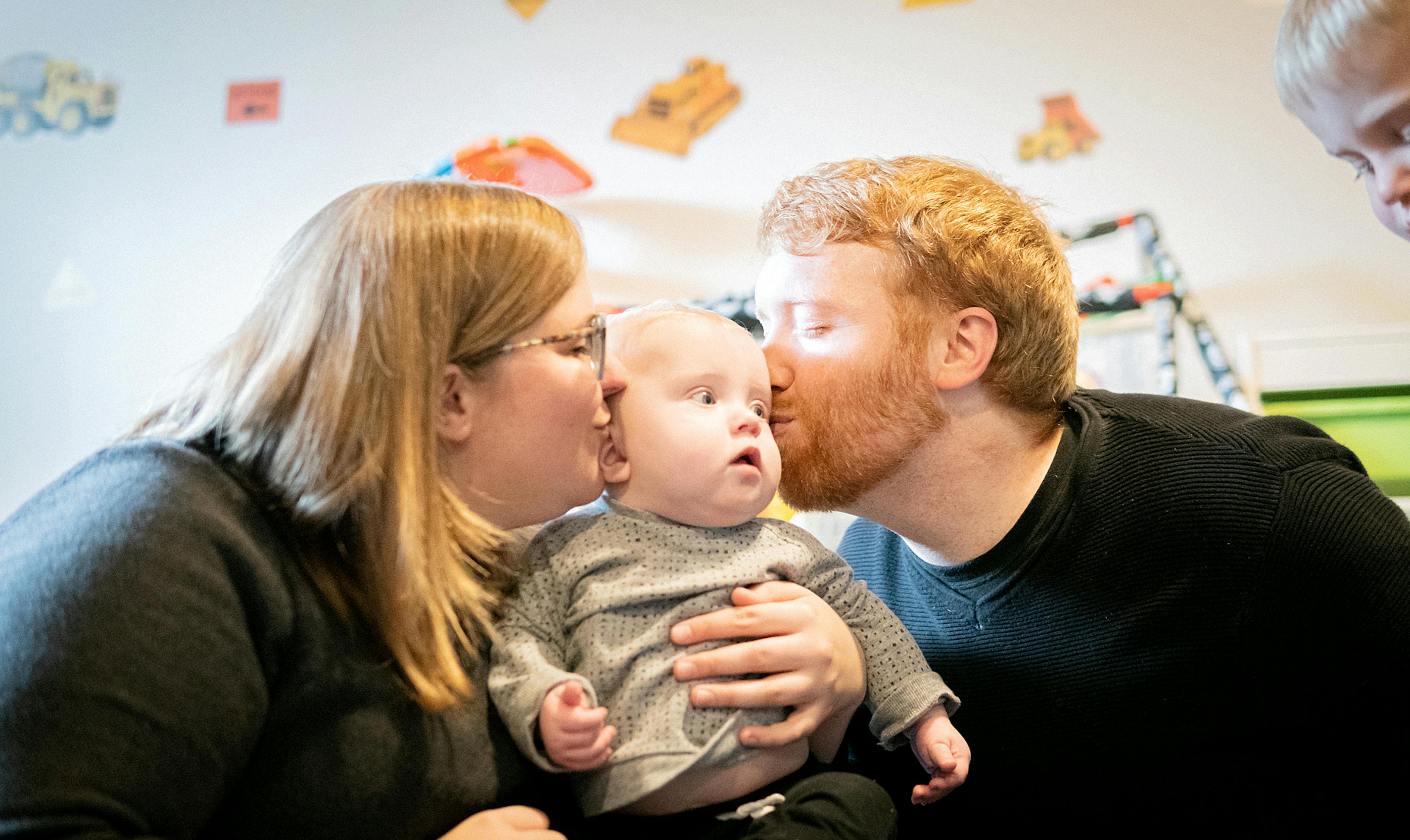 man and woman kiss baby on cheeks