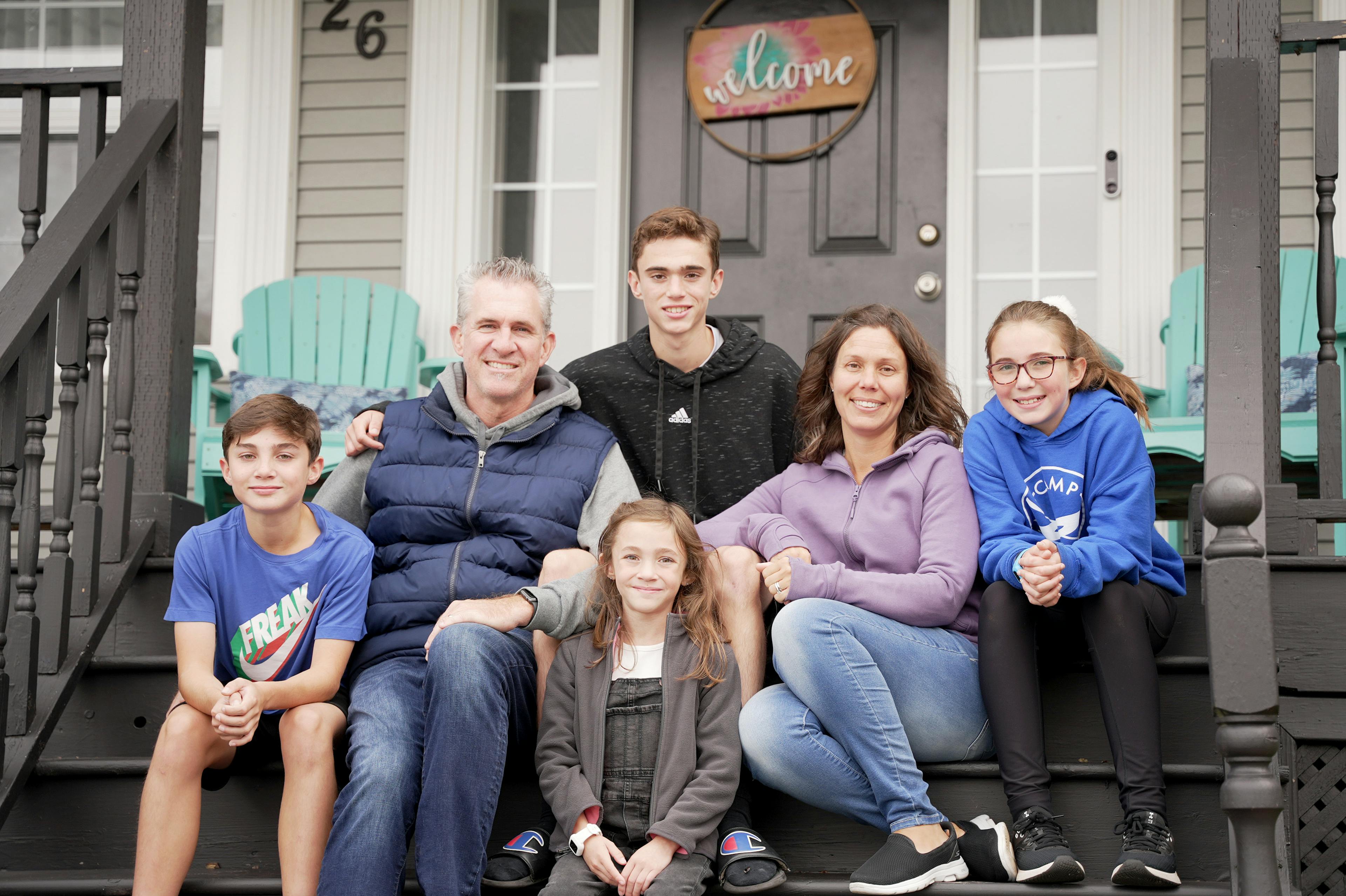 Four children and two adults sit together on their front porch