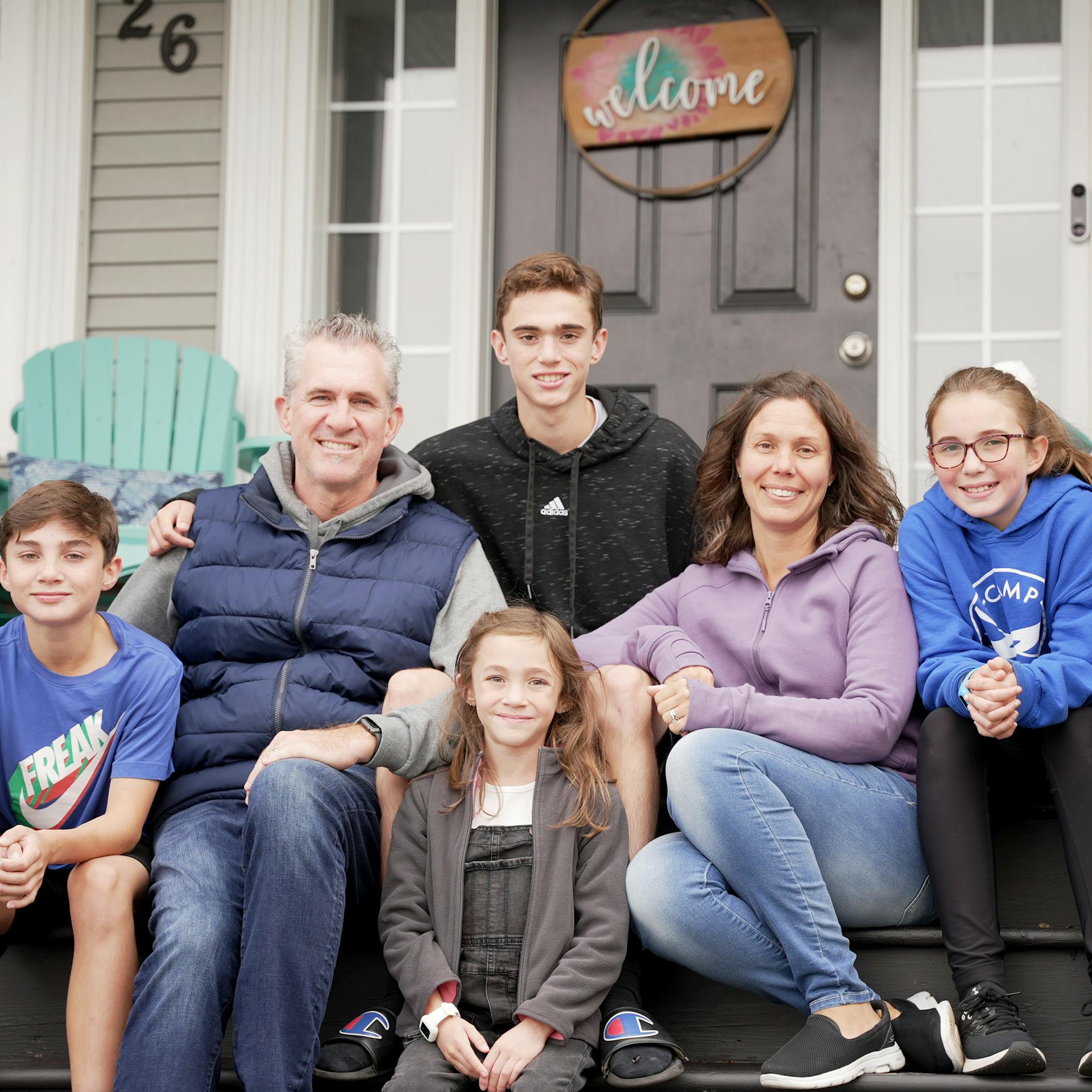 Four children and two adults sit together on their front porch