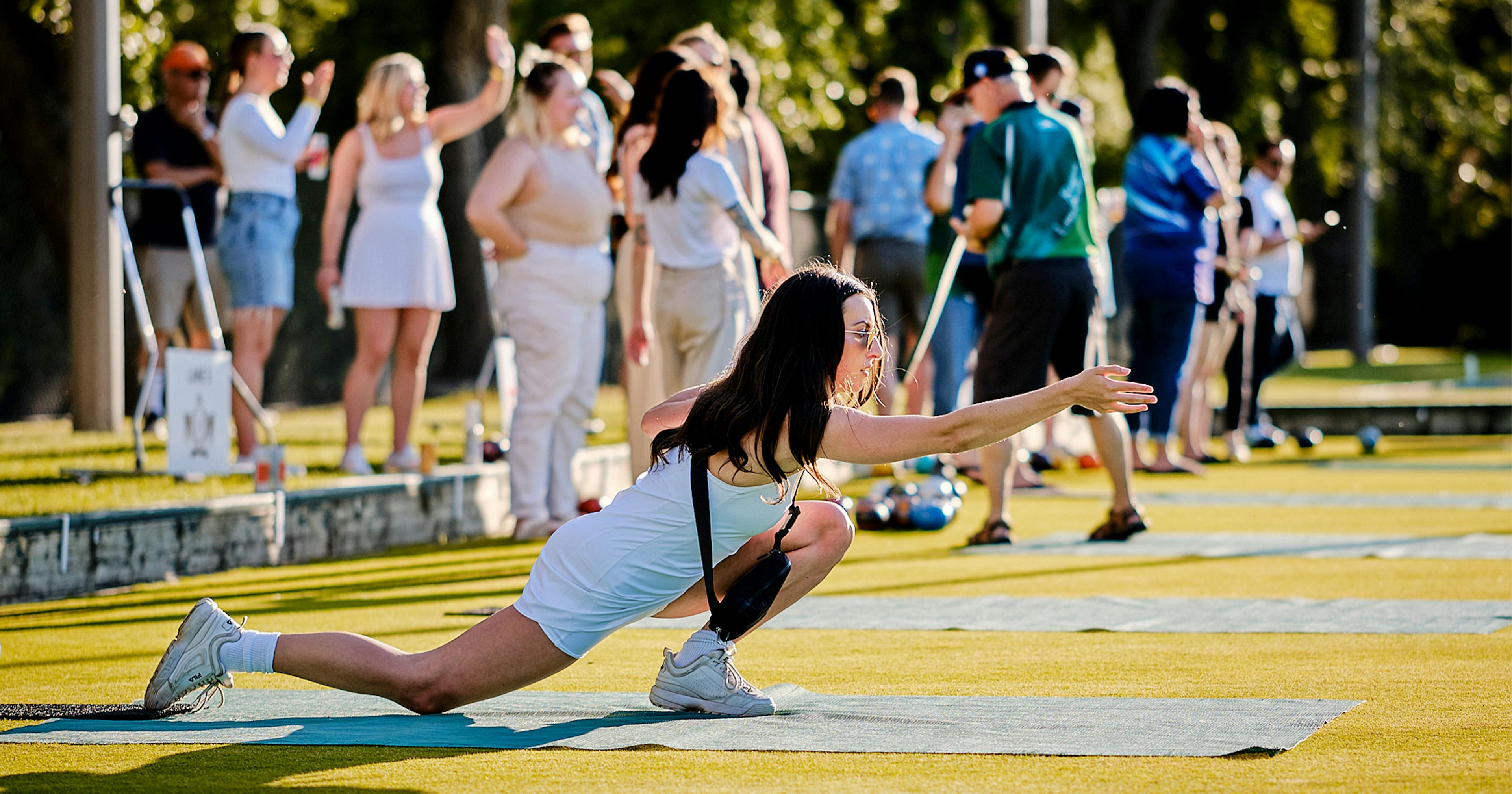 Young woman in deep lunge as she throws a lawn bowling ball.