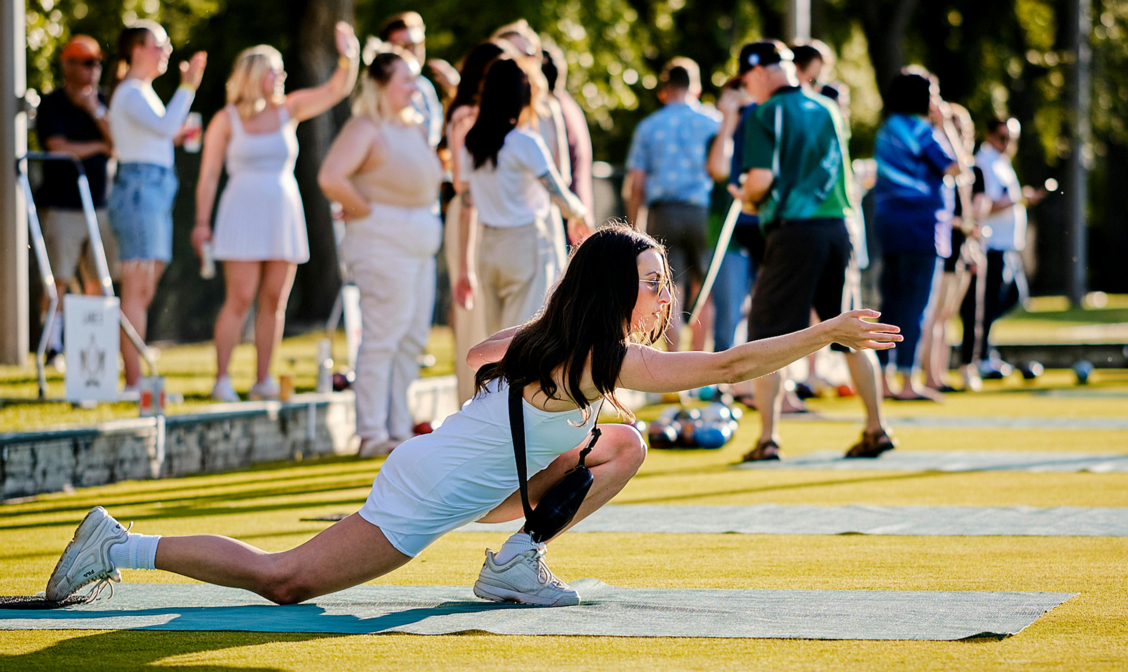 Young woman in deep lunge as she throws a lawn bowling ball.