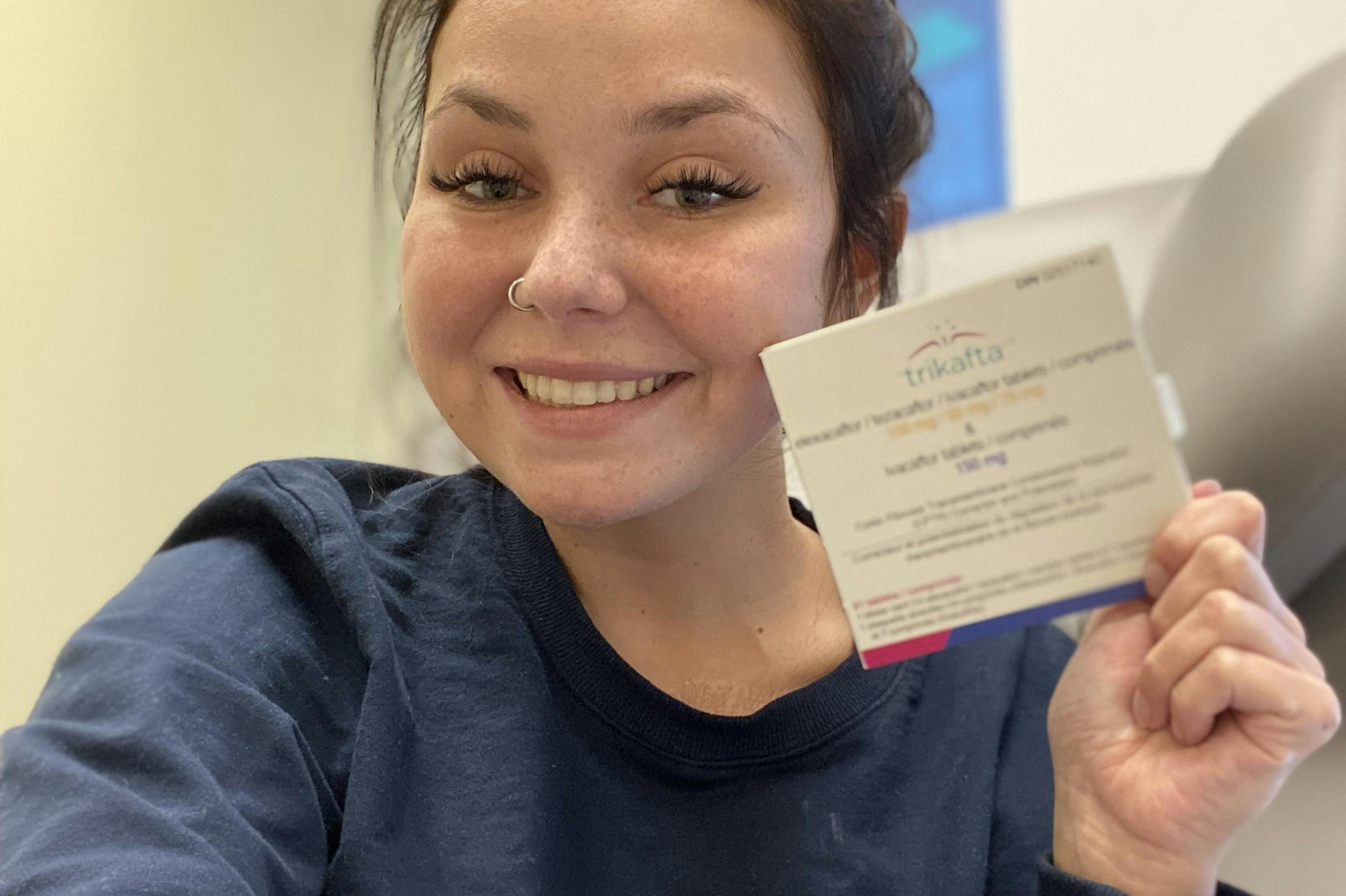 woman smiles and holds up package of Trikafta medicine