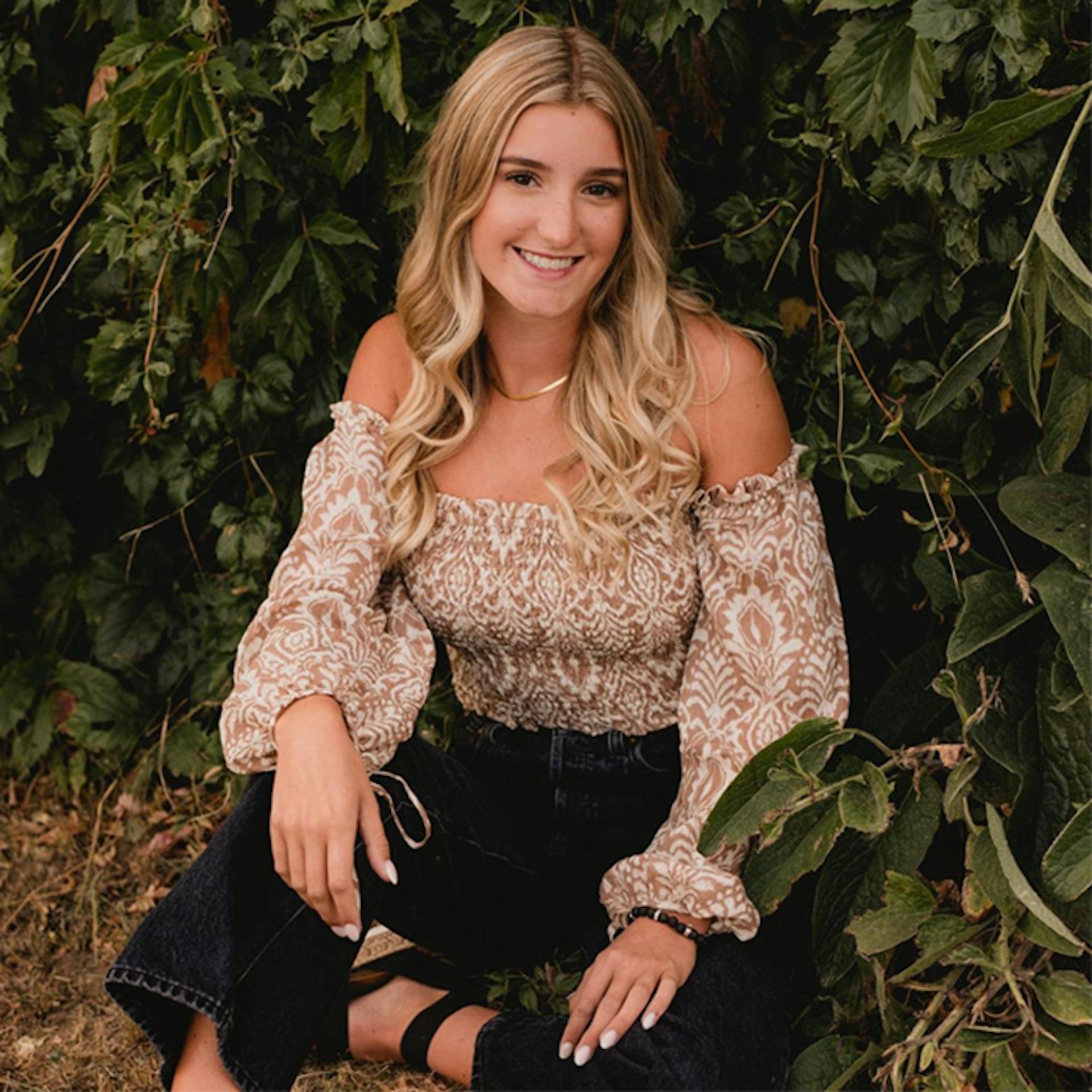 young woman sitting outdoors in front of a tree.