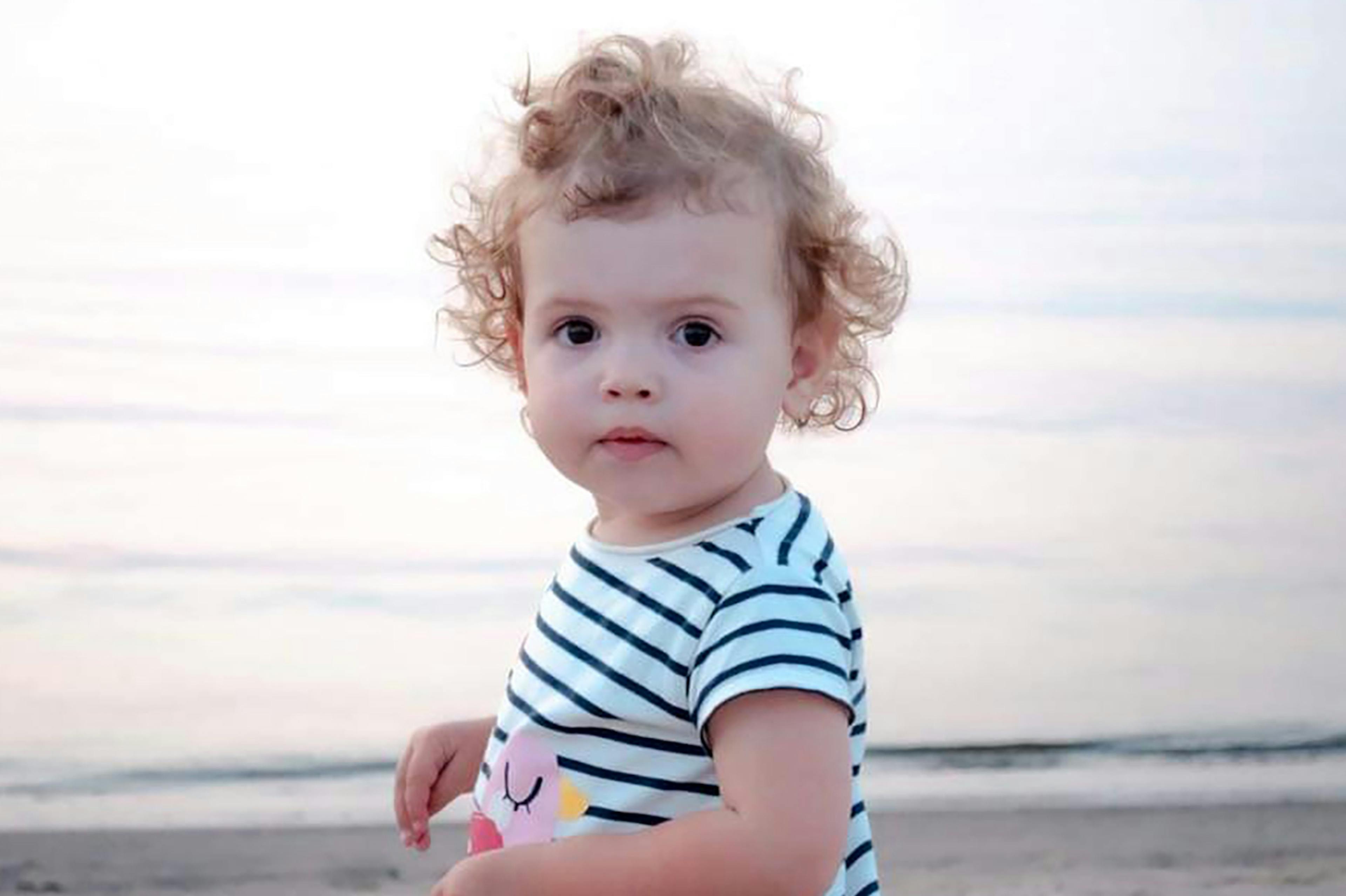 toddler stands on beach and looks at camera