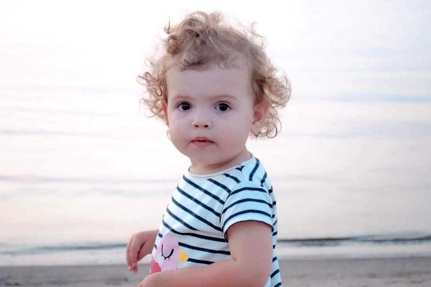 bambin debout sur une plage regardant la caméra