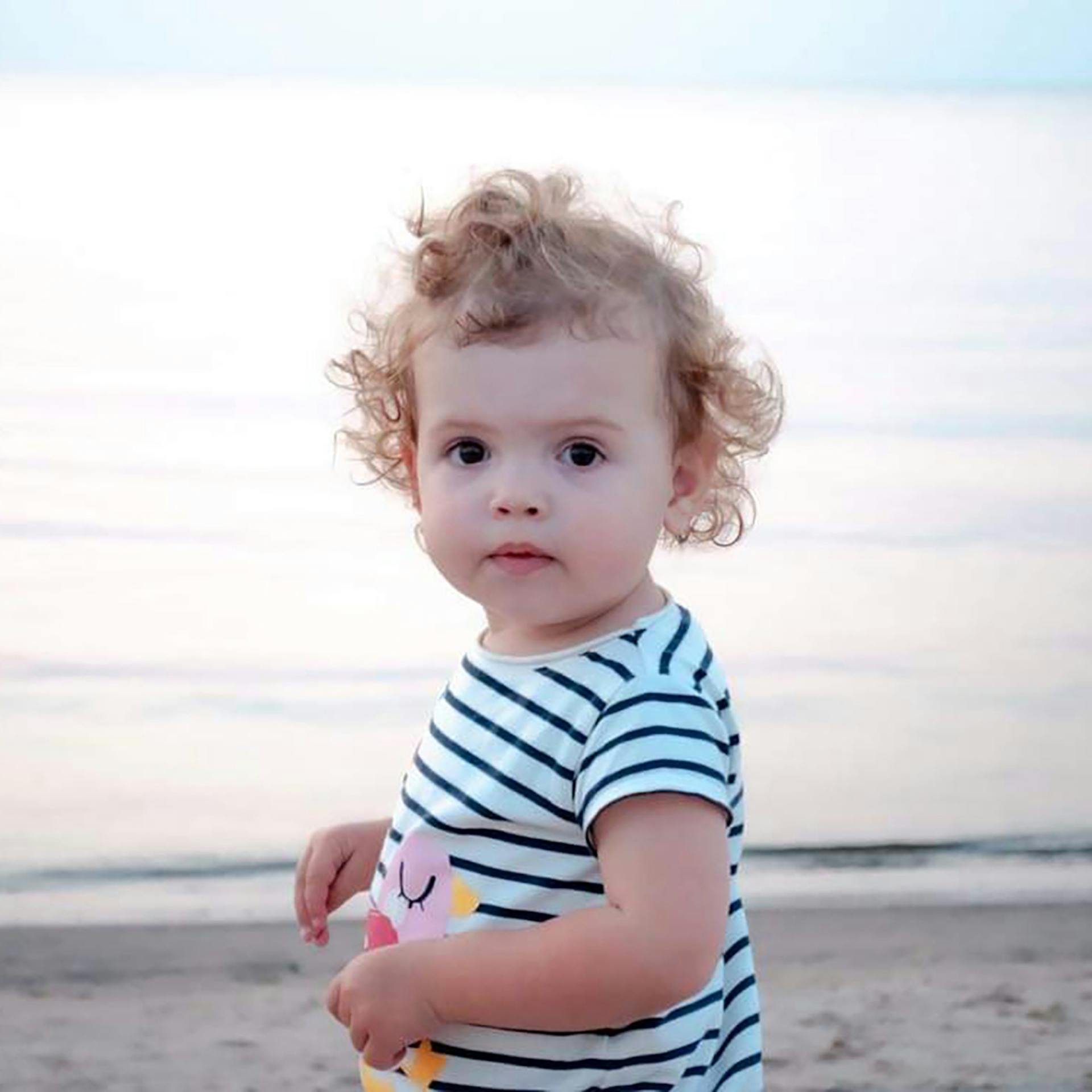 toddler stands on beach and looks at camera