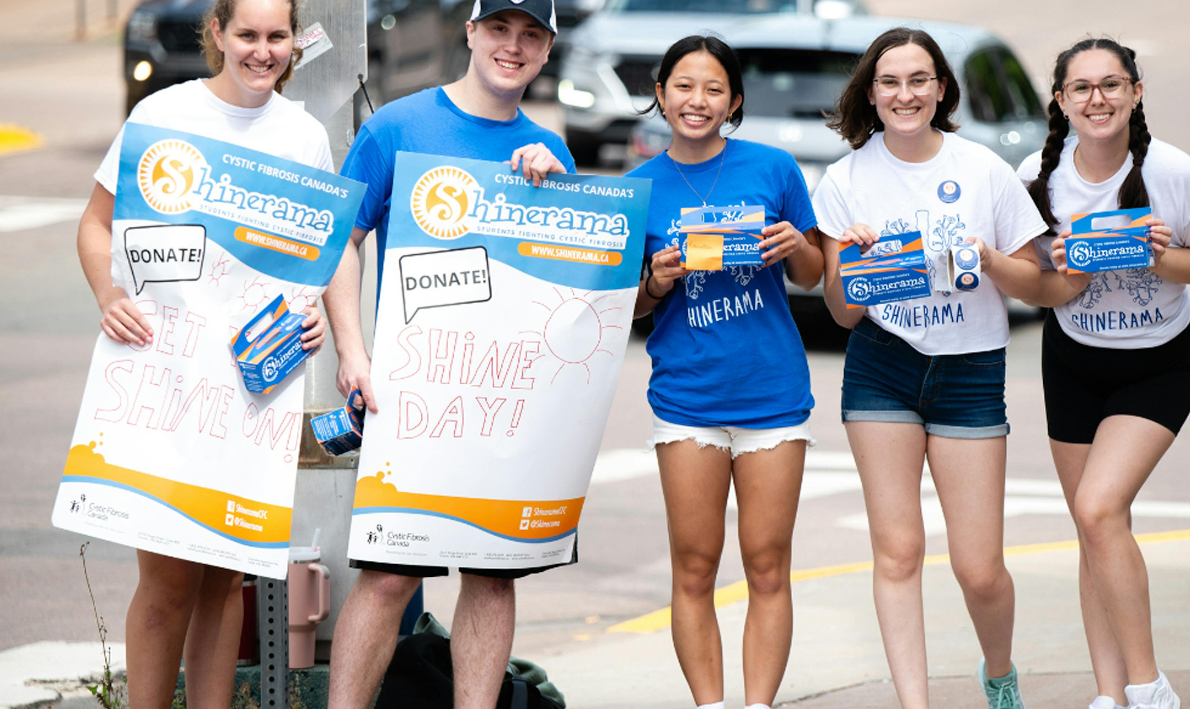 A group of University students hold up Shine promotion posters