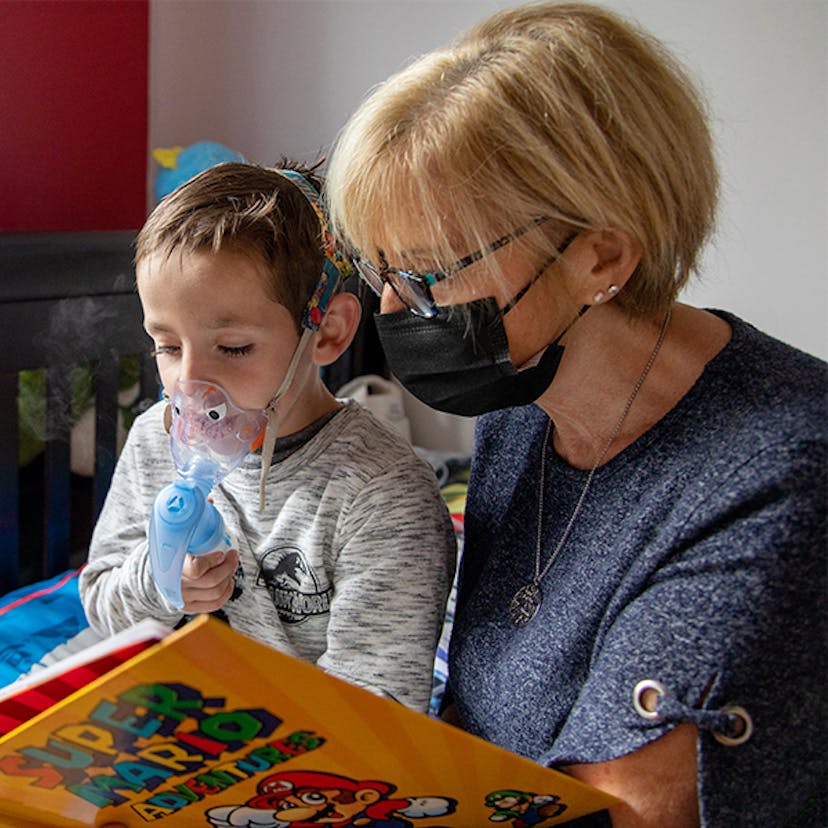 A grandmother reads to her grandson while he uses his nebulizer