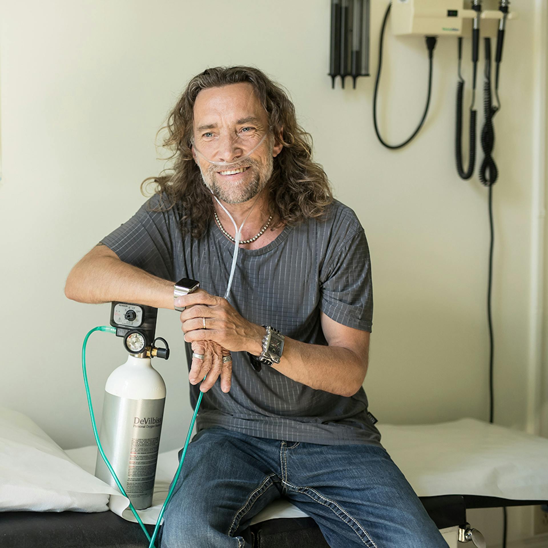 man in doctor's office leans on oxygen tank