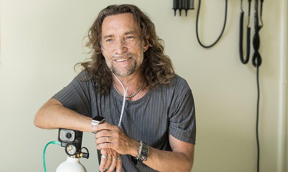 man in doctor's office leans on oxygen tank