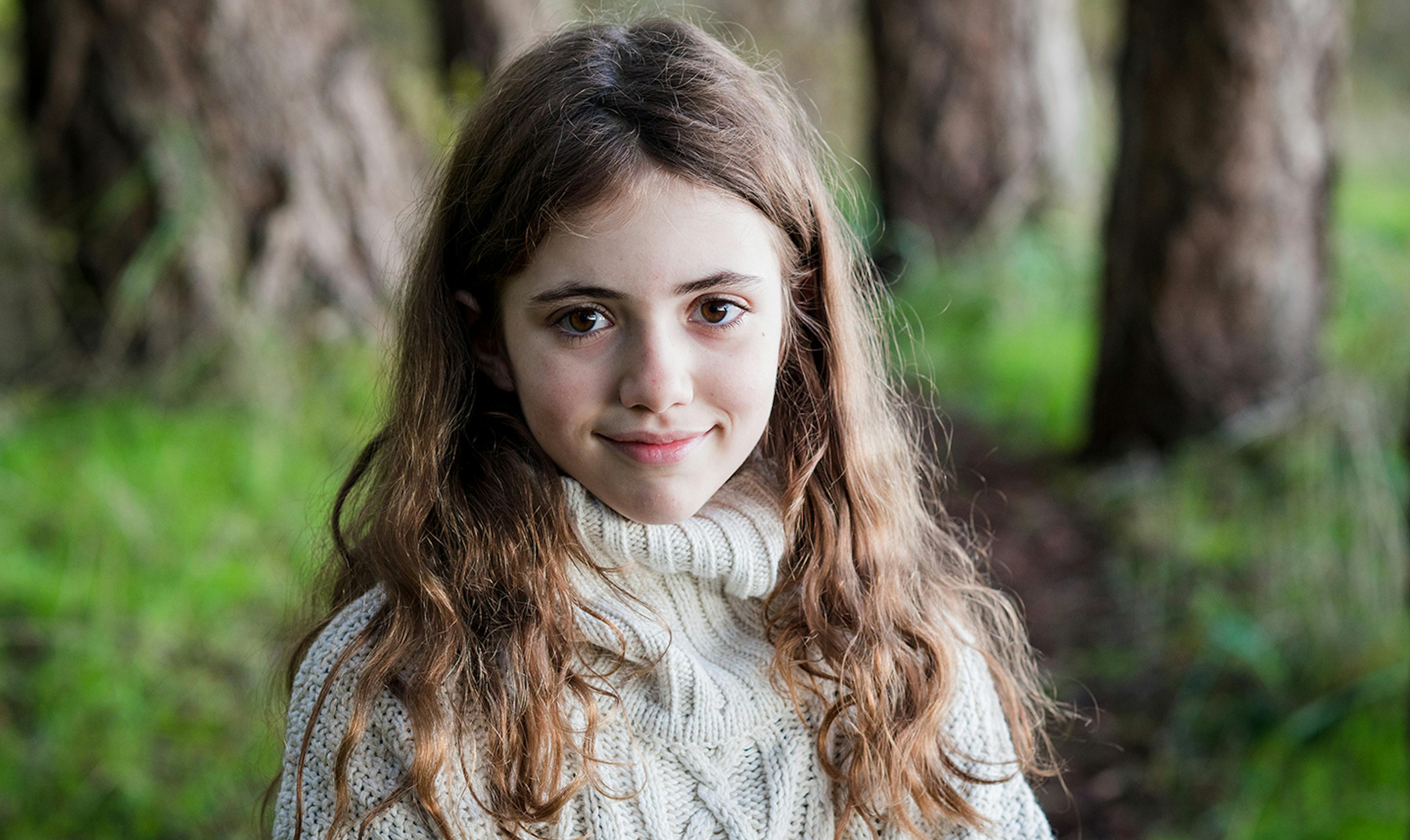 Young girls stands in forest and smiles at camera