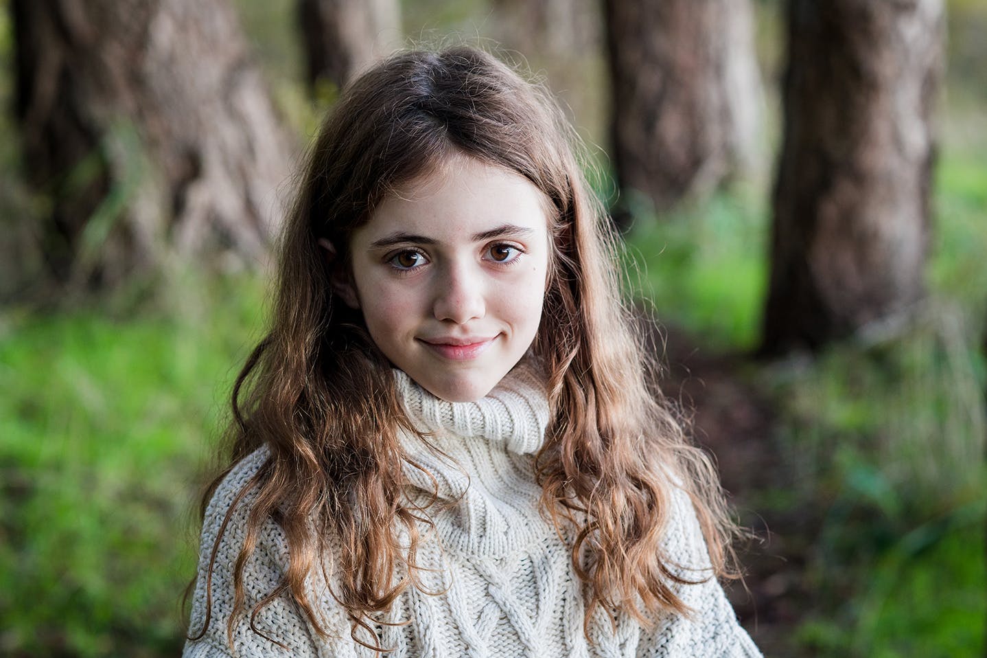 Young girls stands in forest and smiles at camera