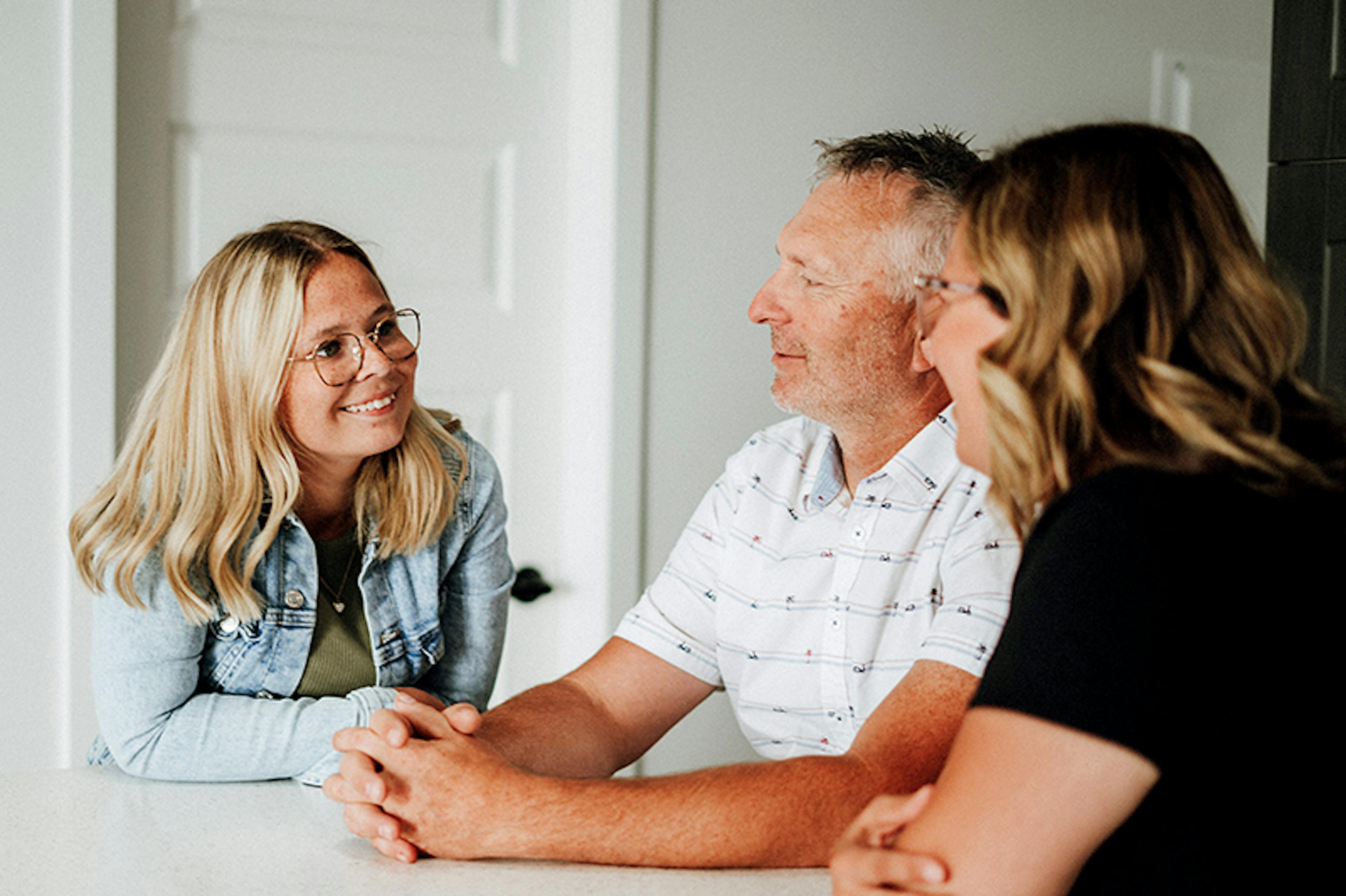 Young woman sits at table and smiles at parents