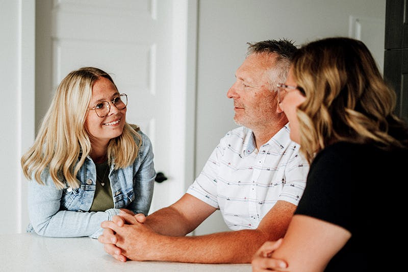 Young woman sits at table and smiles at parents