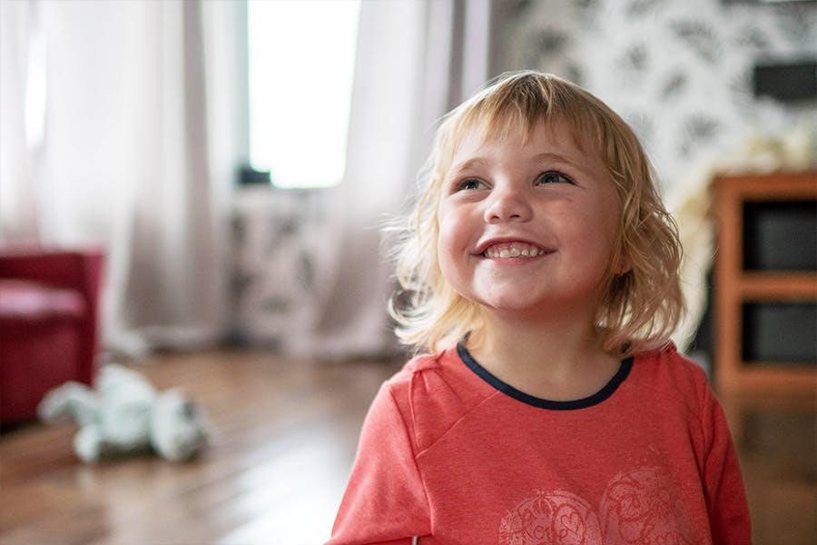A young girl smiles in the sunshine in her bedroom