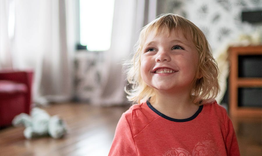 A young girl smiles in the sunshine in her bedroom