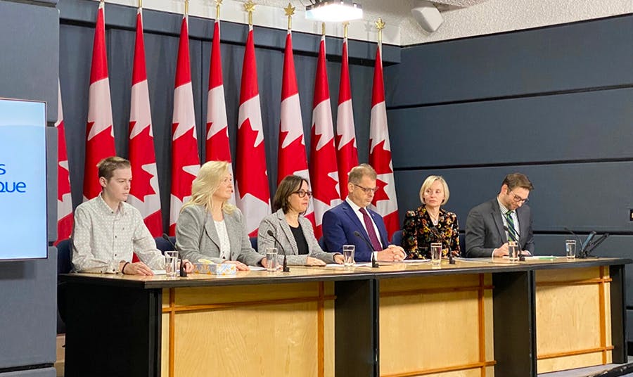Panelists sit at table in front of Canadian flags