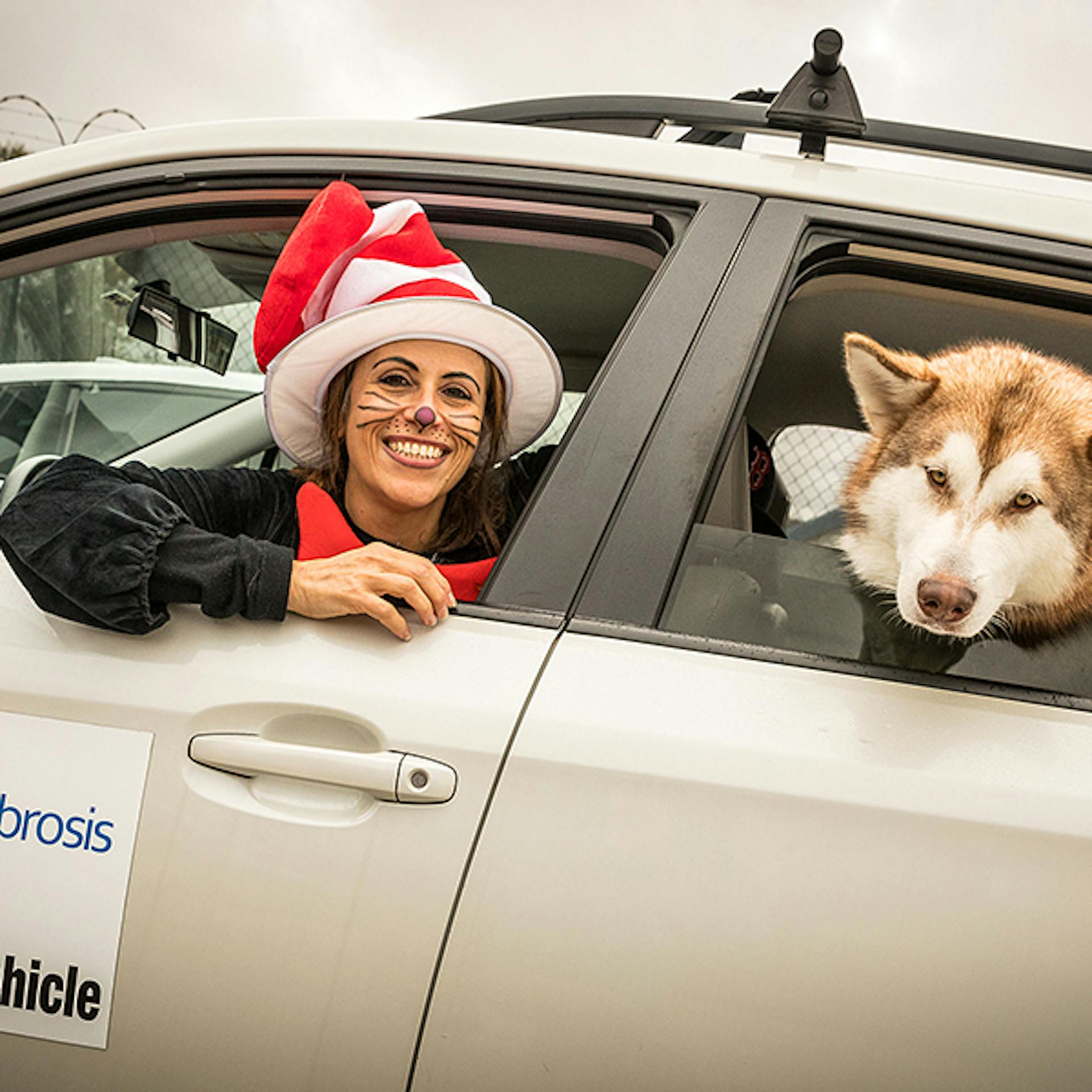 A woman in costume and her dog in a car at a local event