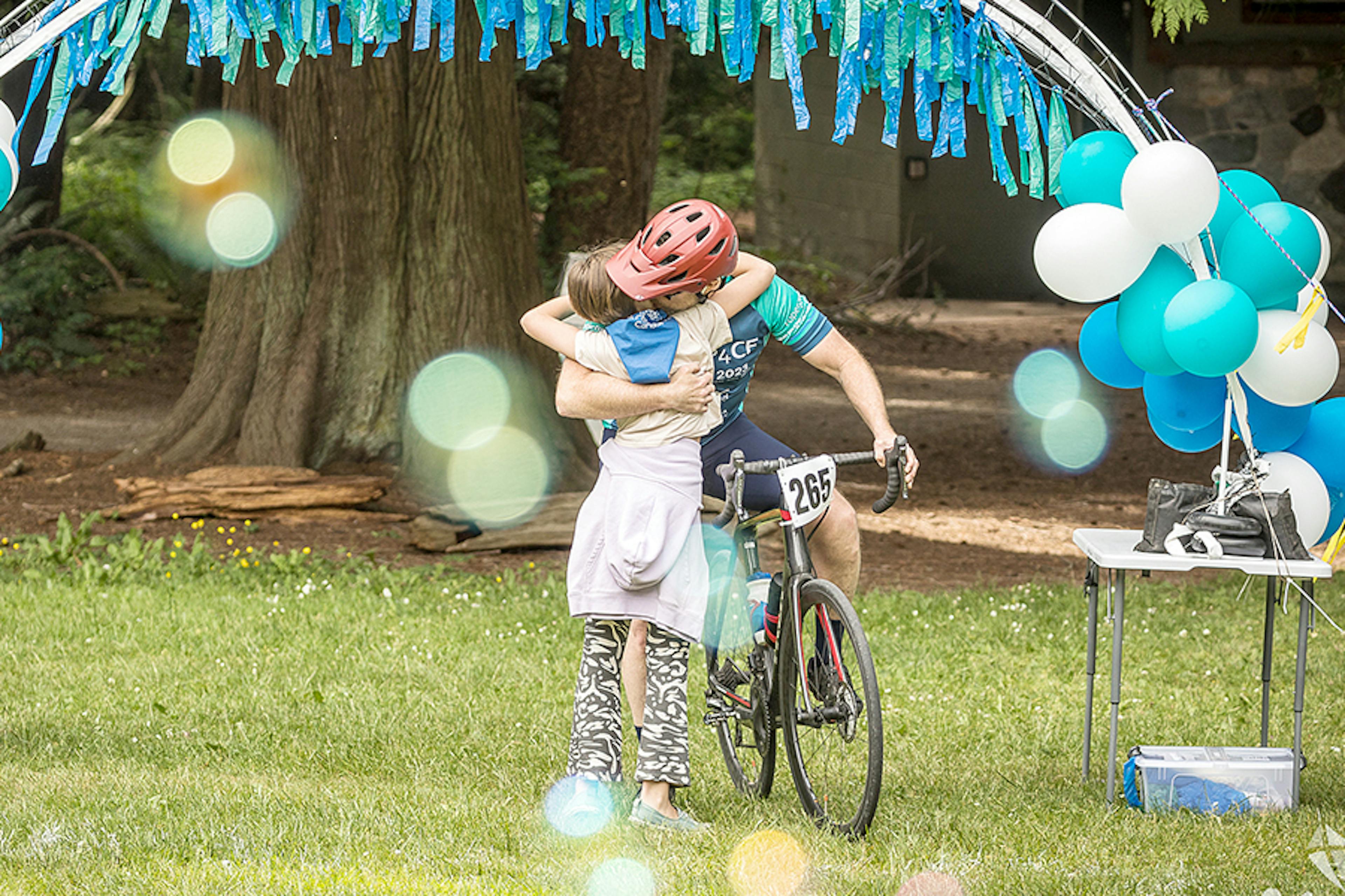 Man on bicycle embraces young girl at CF fundraising event