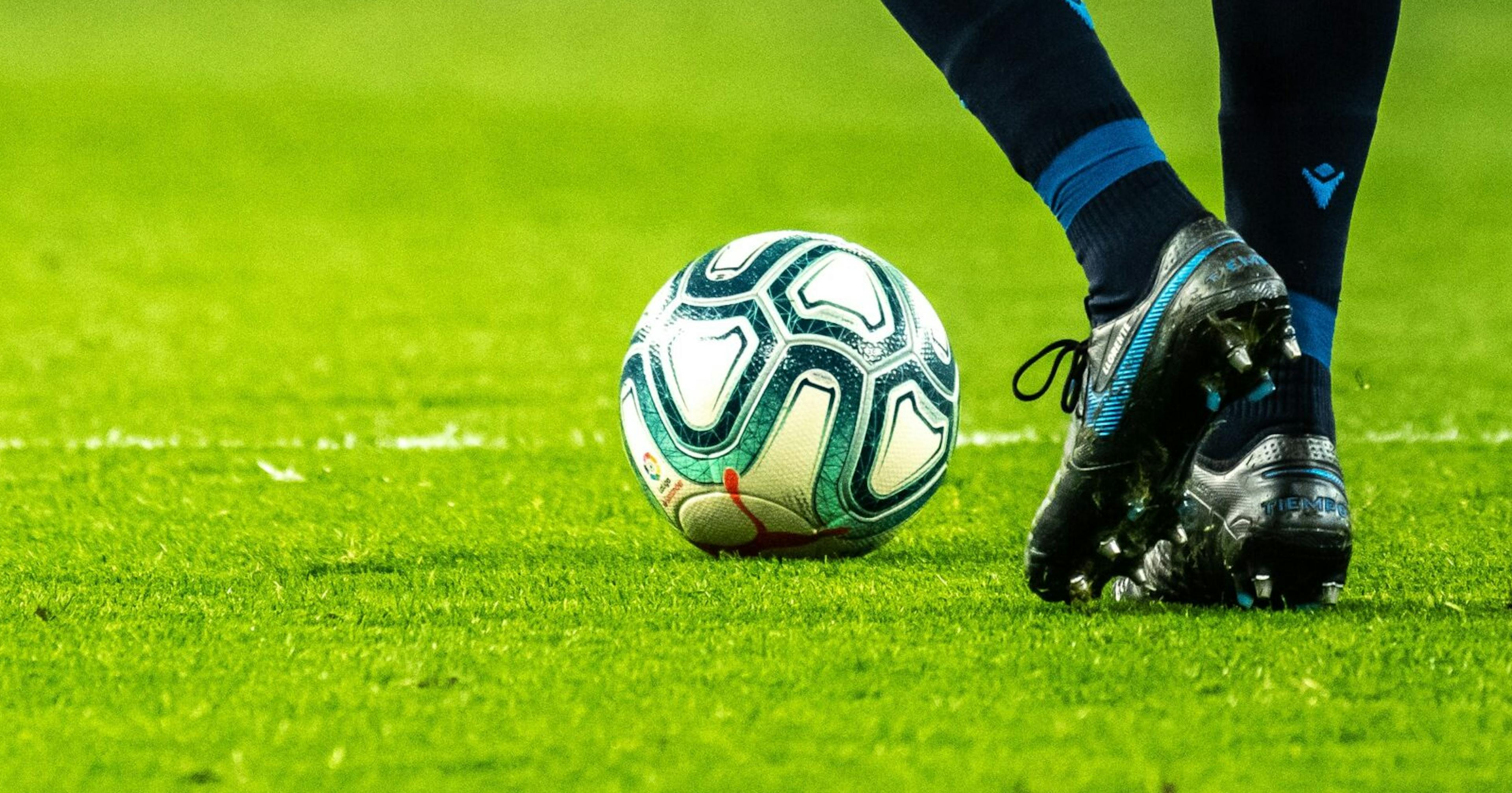 Close up shot of soccer players feet kicking the ball down a bright green field. 