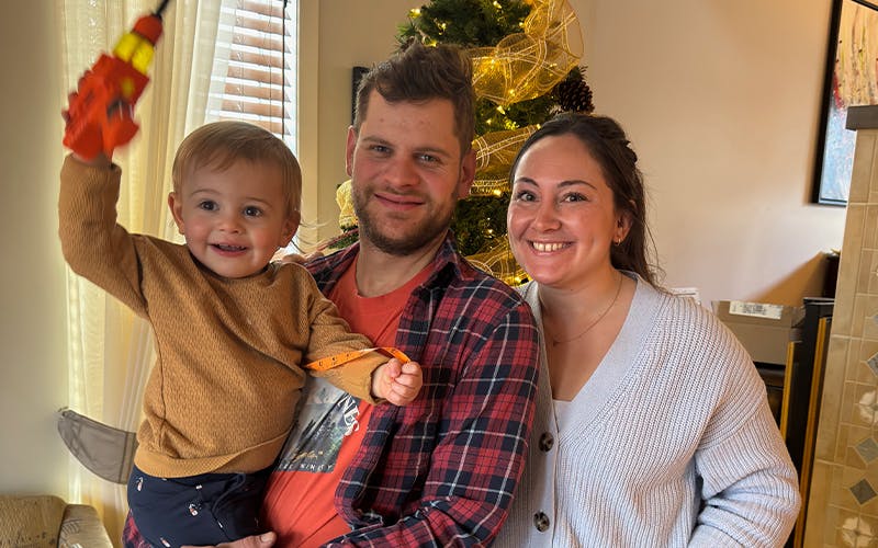 deux parents et un bébé devant un sapin de Noël