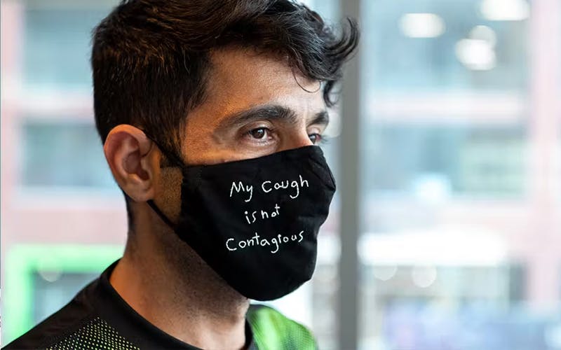 Man wearing a mask that says, "My cough is not contagious".