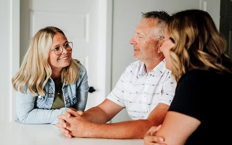 Une jeune femme atteinte de fibrose kystique discute avec ses parents à la table de la cuisine.