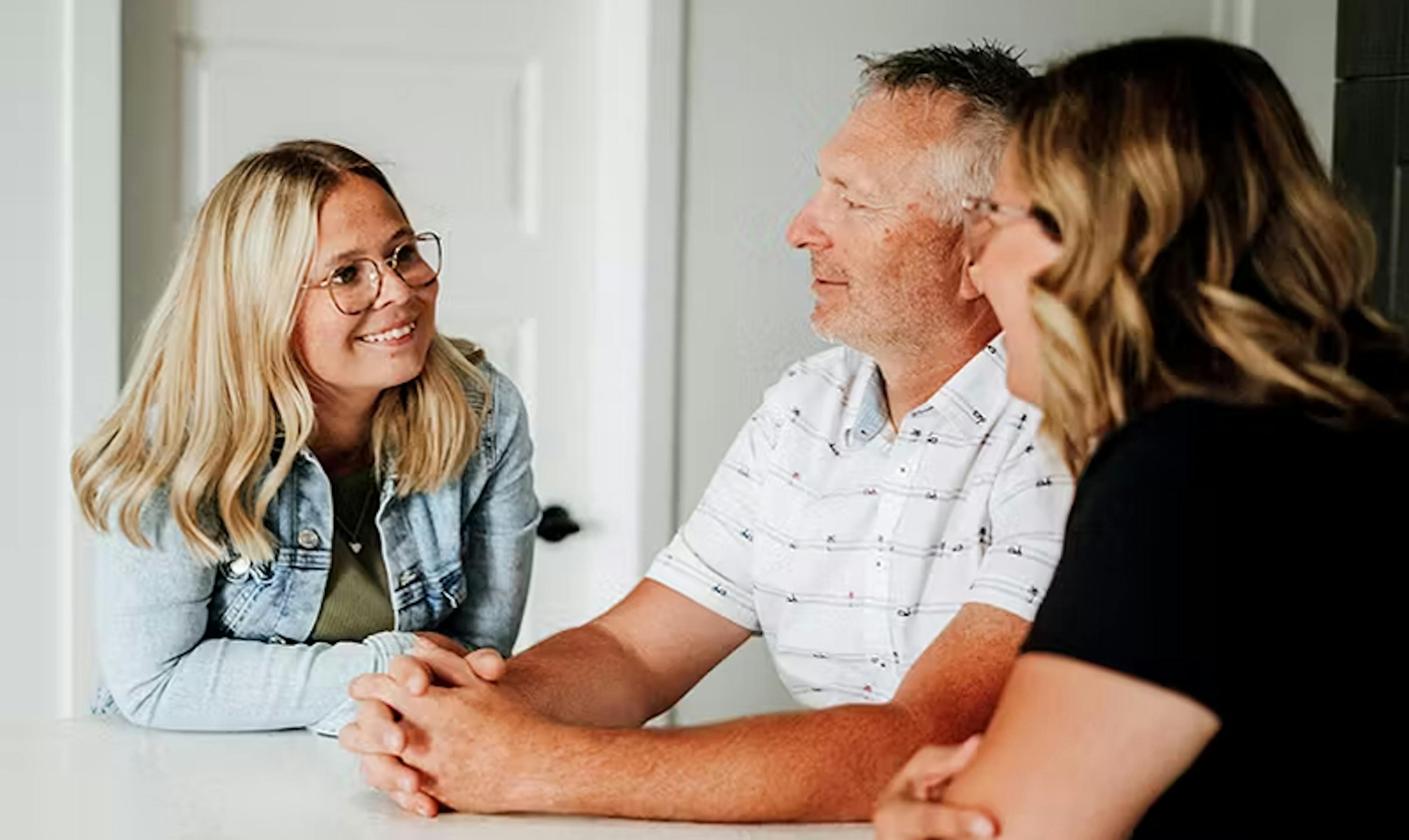 Une jeune femme atteinte de fibrose kystique discute avec ses parents à la table de la cuisine.