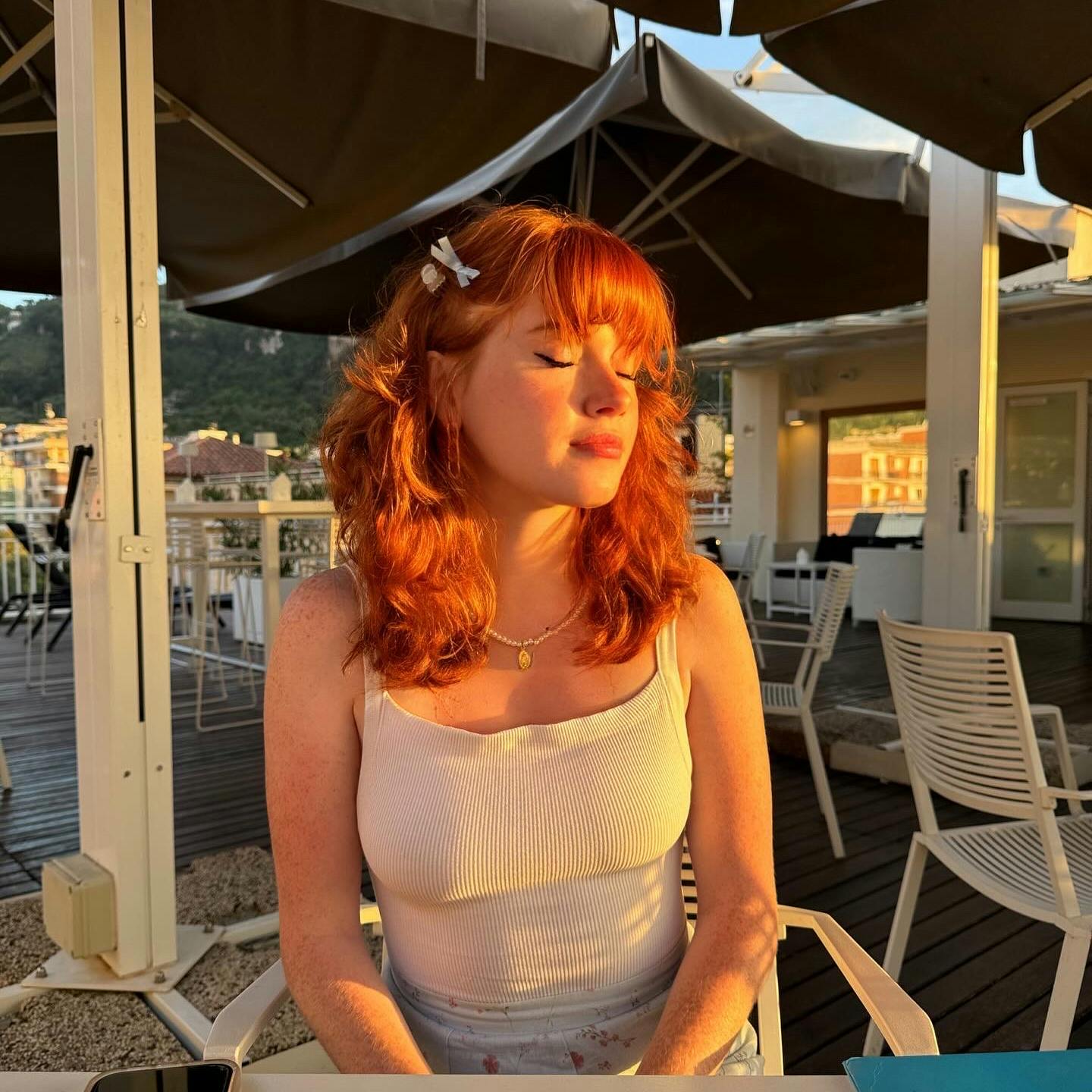 A woman with red hair sitting in a restaurant with her eyes closed.