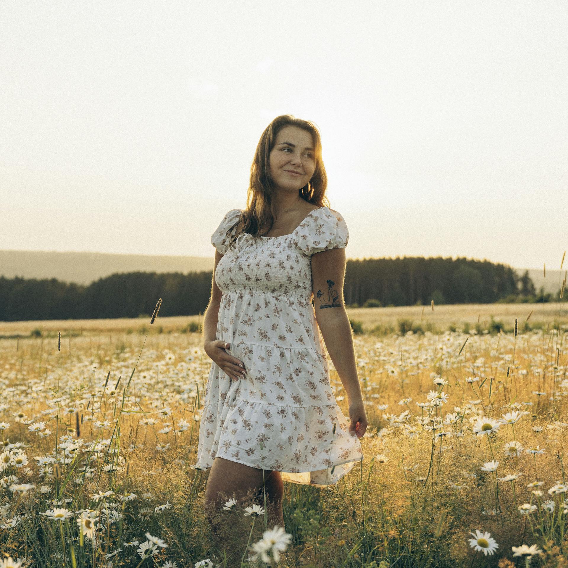 A brunette woman wearing a floral dress in a field.