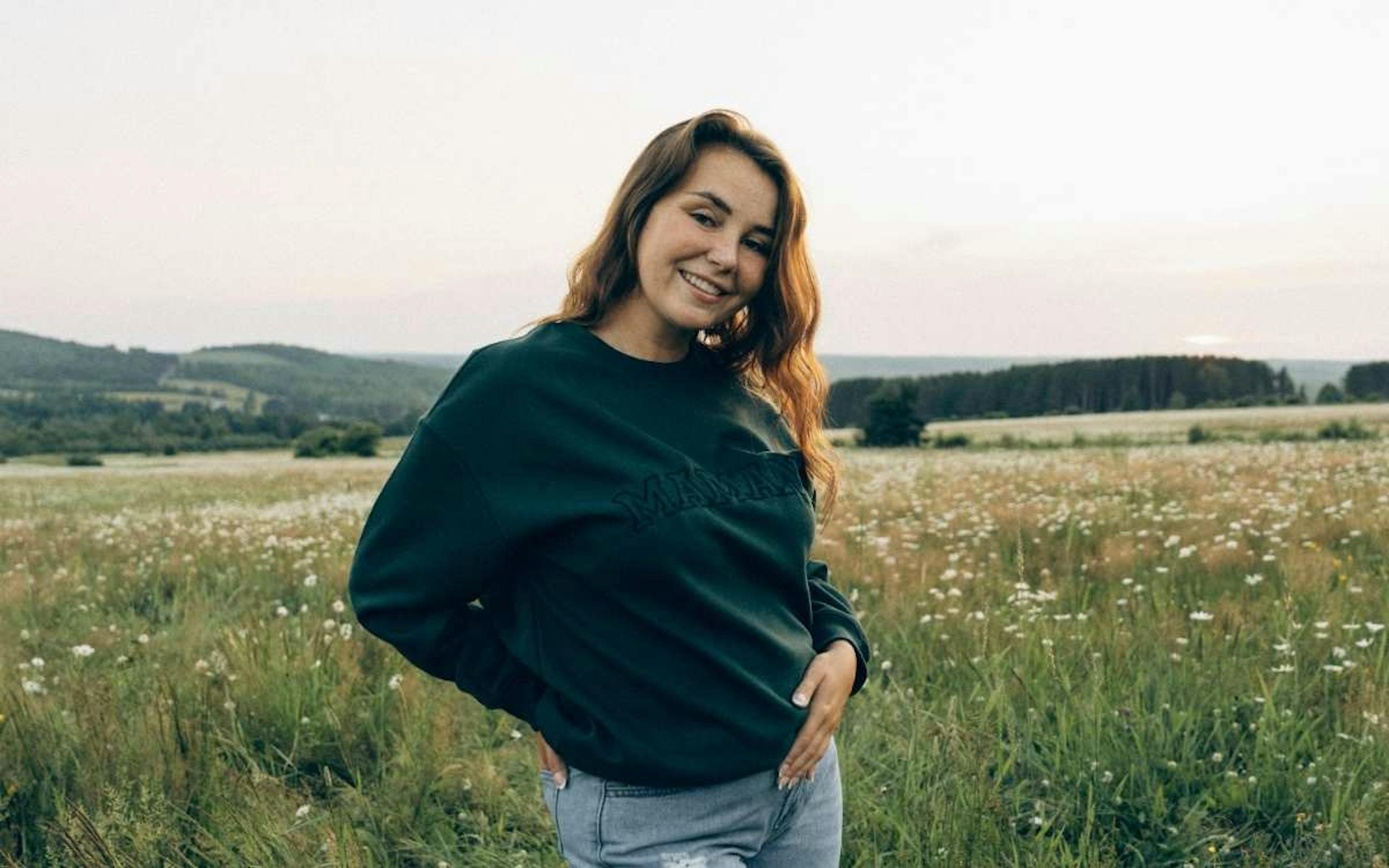 Une femme brune souriant dans un champ.