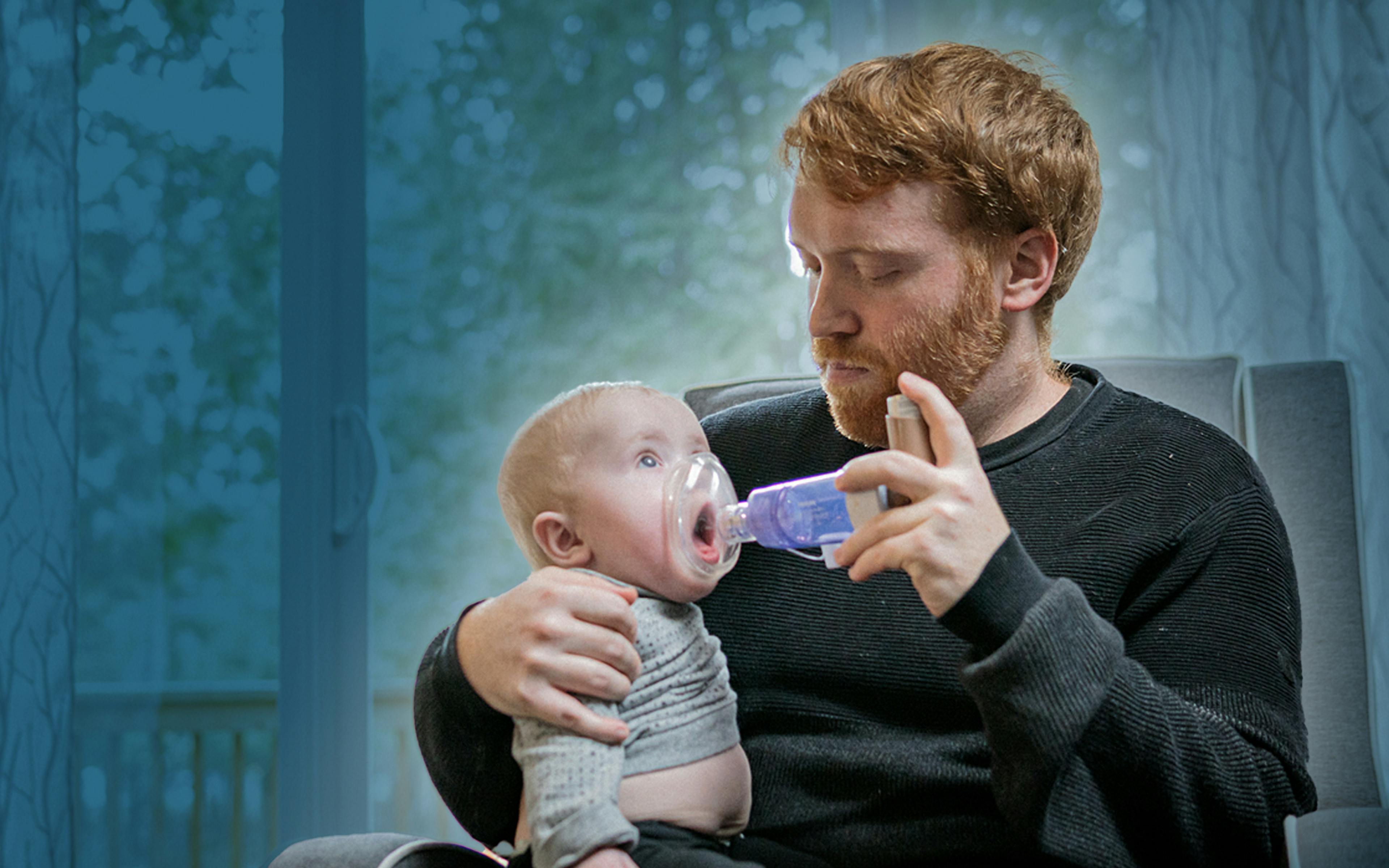 A young father cradles his infant son who is using a nebulizer.