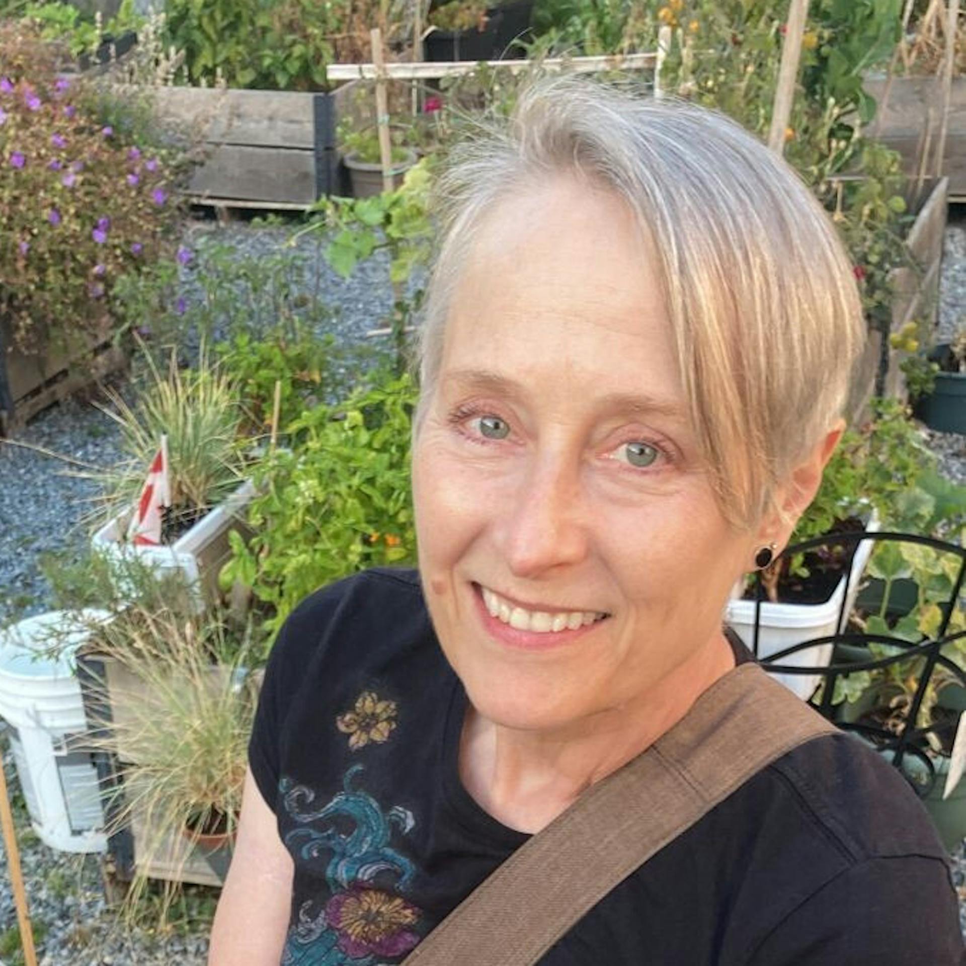 Une femme souriante aux cheveux blonds courts dans un jardin.