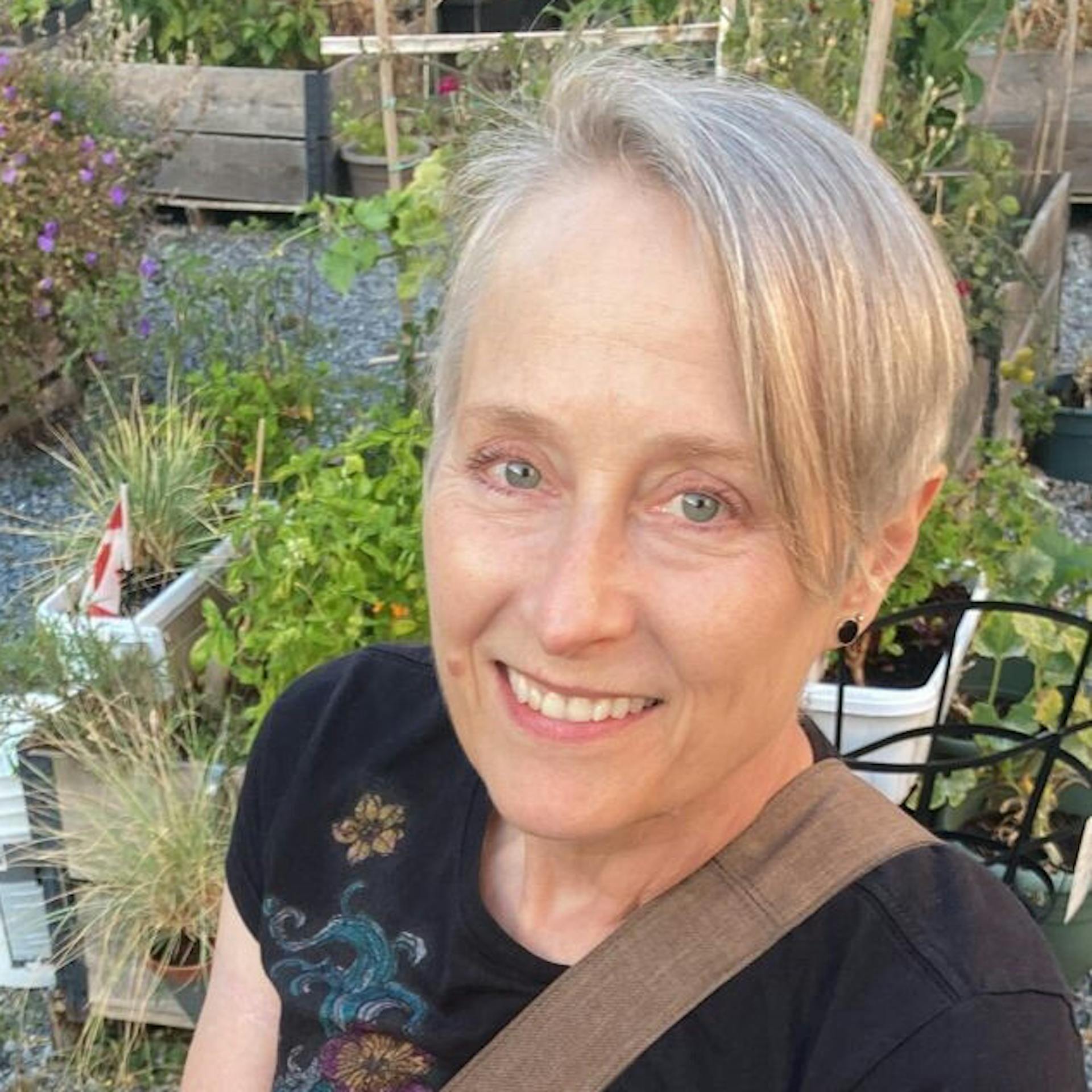 A smiling woman with short blonde hair in a garden.
