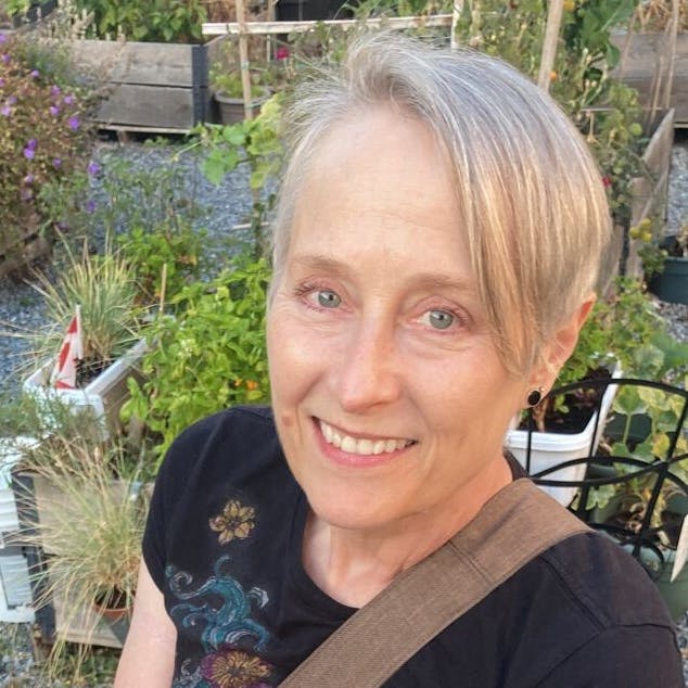 A smiling woman with short blonde hair in a garden.
