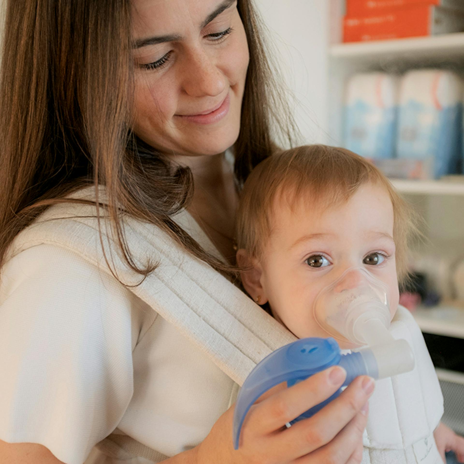 Une jeune maman tient son bébé dans un porte-bébé tout en l'aidant à utiliser son nébuliseur.