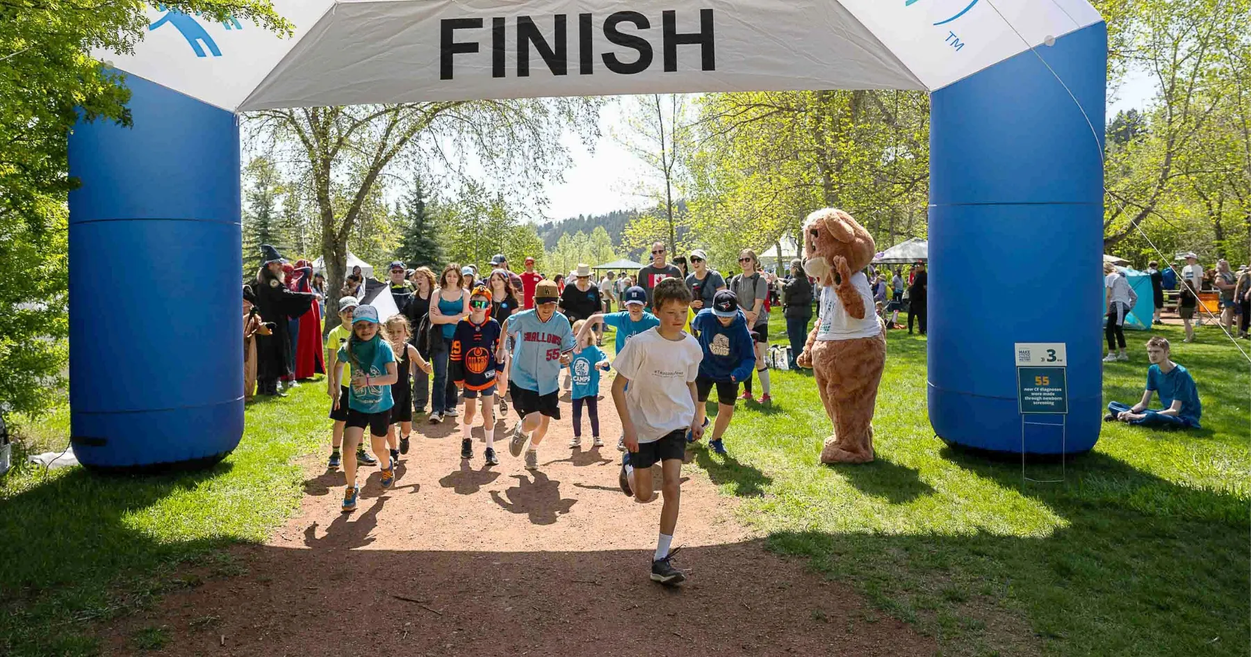 A large group of children run through the finish line at The Walk to Make Cystic Fibrosis History