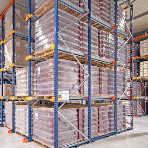 3 rangées de rack à palettes dans un entrepôt  avec des cartons dessus