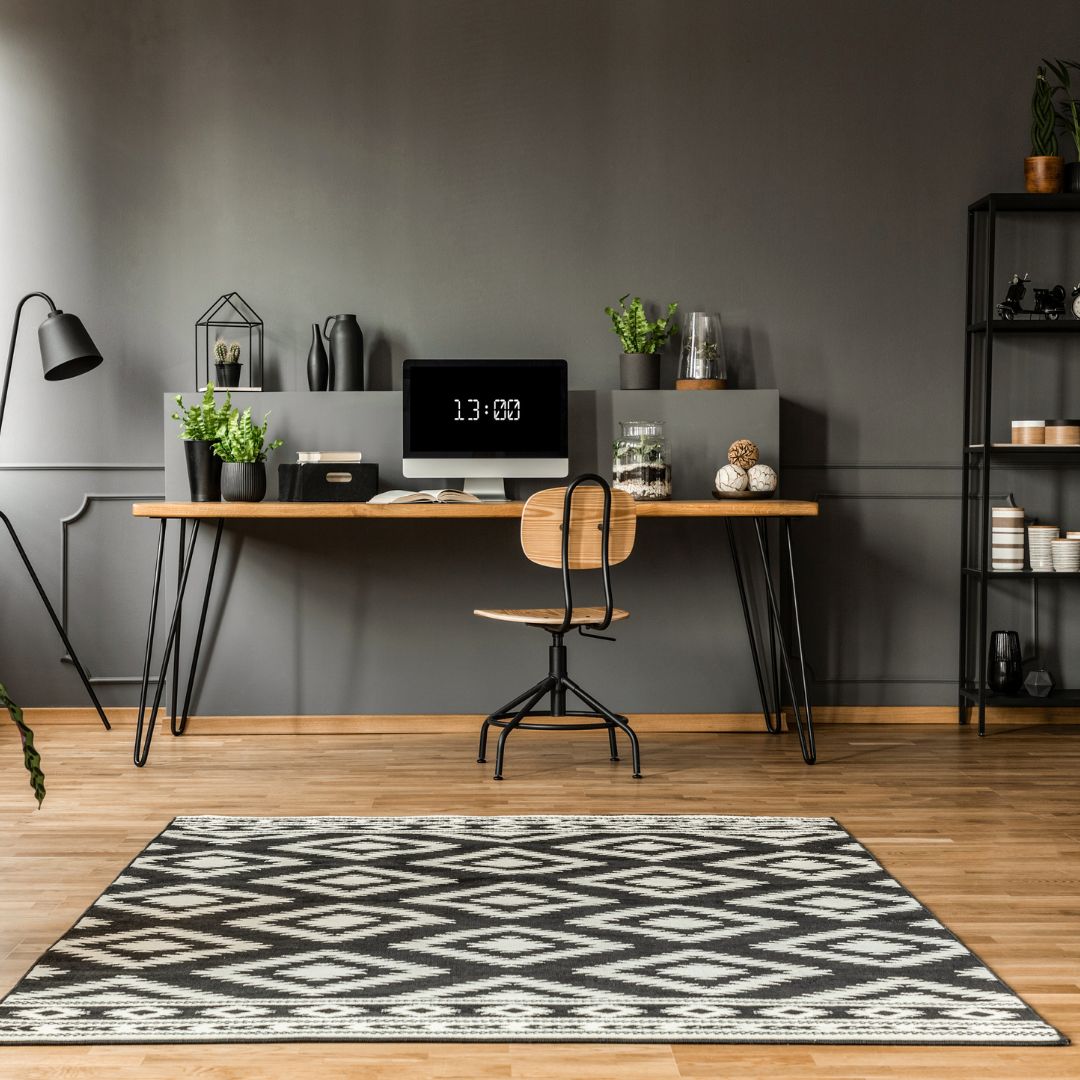 Un salon avec un bureau, une chaise, un tapis, un ordinateur et une plante