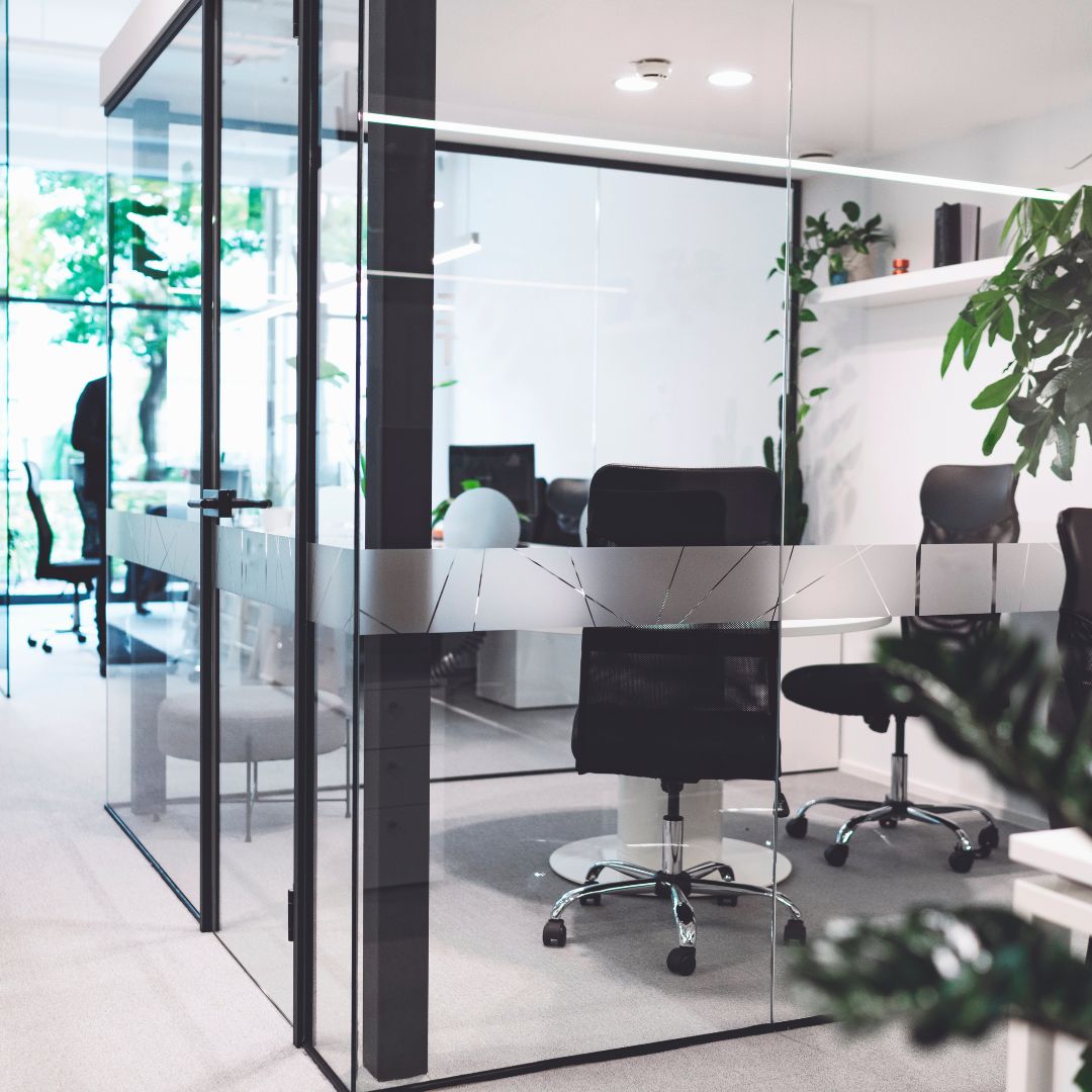 Un espace de travail isolé de la pièce par une verrière avec des plantes, une table et des chaises