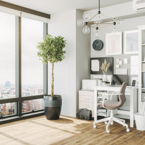 Un salon avec des grandes fenêtres, une plante, un bureau et une chaise